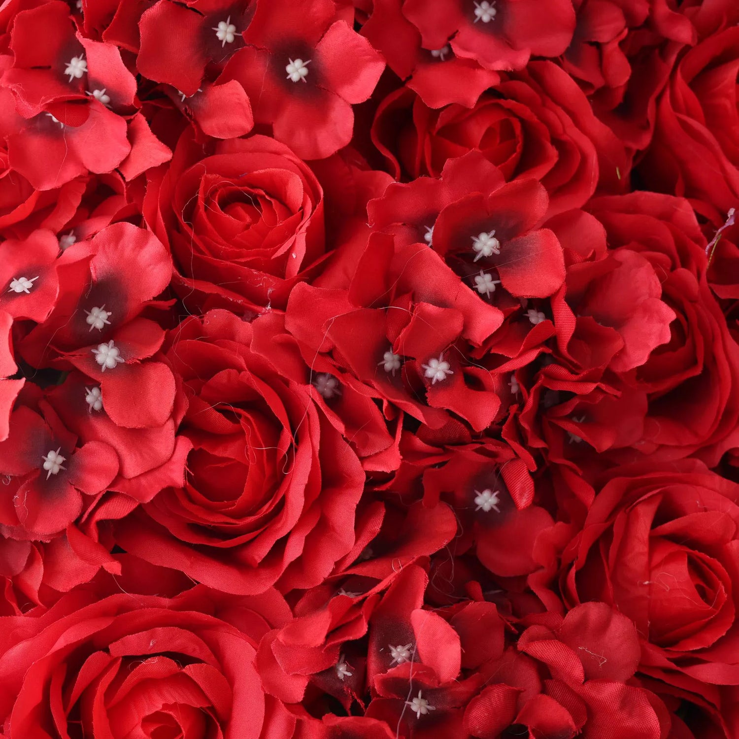 This close - up showcases a lush artificial flower wall. It features vibrant red roses and small blossoms with white centers. The dense, uniform arrangement creates a bold, passionate, and elegant texture. Ideal as a backdrop for events like weddings, it adds drama and romance, enhancing the atmosphere with its rich color and intricate floral design.
