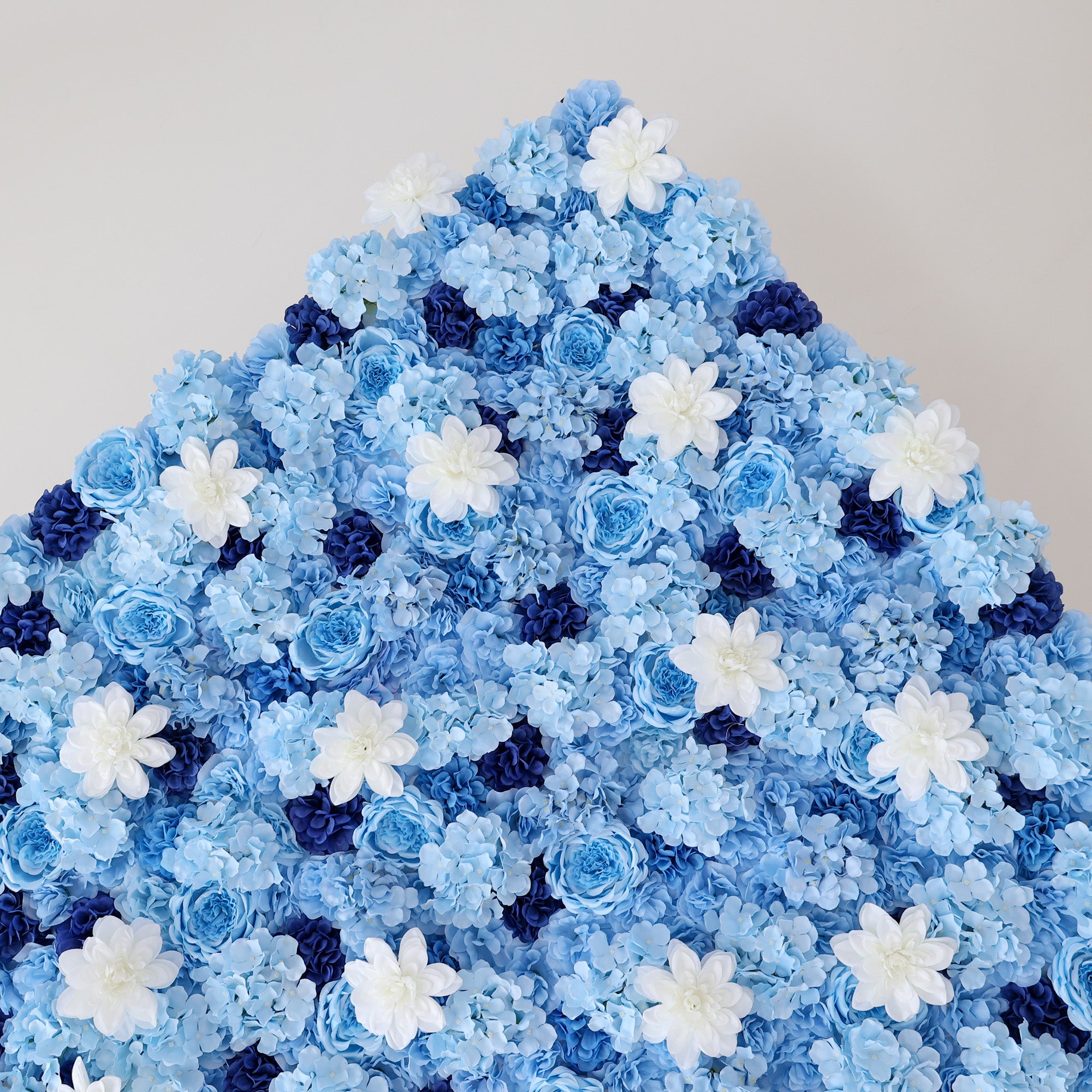 A large, triangular artificial flower arrangement showcases soft blue hydrangeas, blue roses, dark blue blossoms, and white daisy - like flowers. The dense, layered design creates an elegant, serene backdrop, perfect for events or decorative spaces, evoking a calm and dreamy ambiance.
