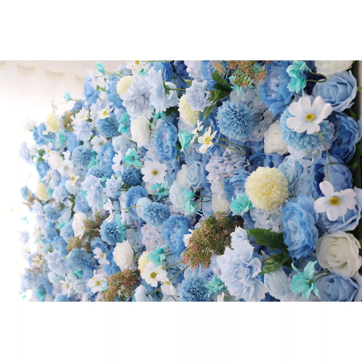 A close - up of an artificial flower wall features a beautiful mix of blue blooms. There are soft - toned roses, fluffy chrysanthemums, delicate daisies with yellow centers, and hints of teal foliage. The varied textures and harmonious blue hues create a lush, elegant and serene floral tapestry, perfect for adding a decorative touch to spaces or events.