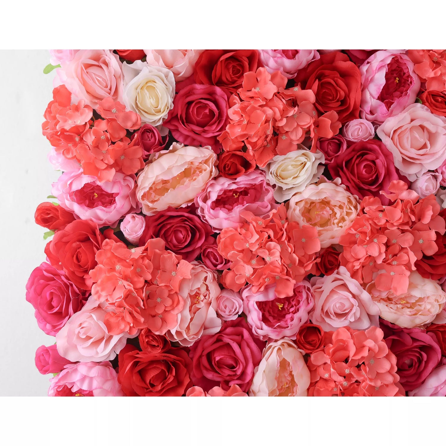 A close - up of a lush artificial flower wall showcases a vibrant mix of roses and hydrangeas. The blooms feature soft pinks, deep reds, and coral hues, with varied petal textures creating a rich, romantic tapestry. Green leaves peek through, adding a natural touch. Perfect for elegant decor, this arrangement exudes warmth and sophistication, ideal for backdrops at weddings or special events.