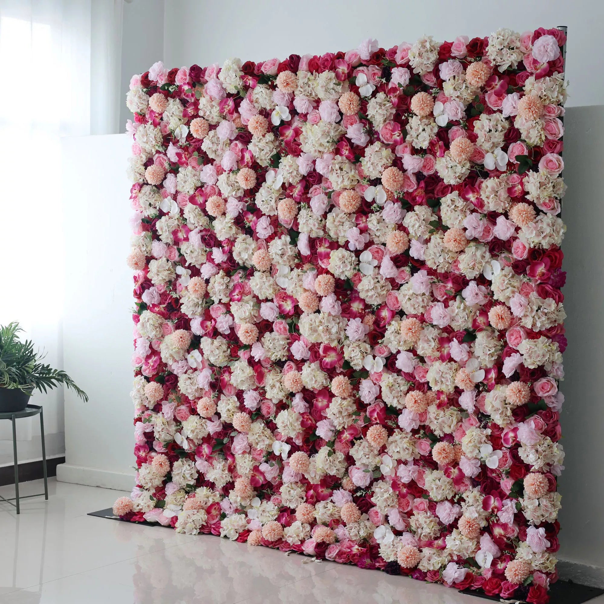 This is a large artificial flower wall. It combines red blossoms with white, pink, and peach - colored blooms, creating a rich, textured display. The dense arrangement of varied flowers, like hydrangeas and roses, forms a vibrant, eye - catching backdrop, perfect for adding an elegant, decorative touch to events such as weddings or parties.