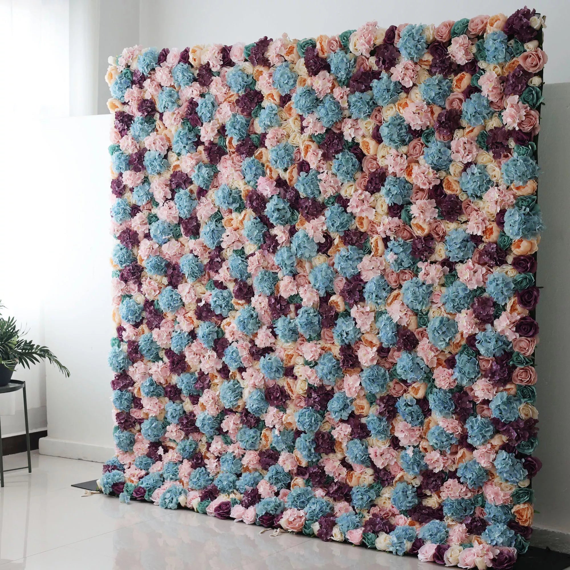 Valar Flowers Roll Up Backdrop: This is a large artificial flower wall. It showcases a vibrant mix of colors—soft pinks, blues, purples, and creams. Densely packed with varied blooms, it creates a lush, textured tapestry. Perfect for event backdrops, adding a colorful, elegant touch to weddings or parties, enhancing the decorative appeal of any space.