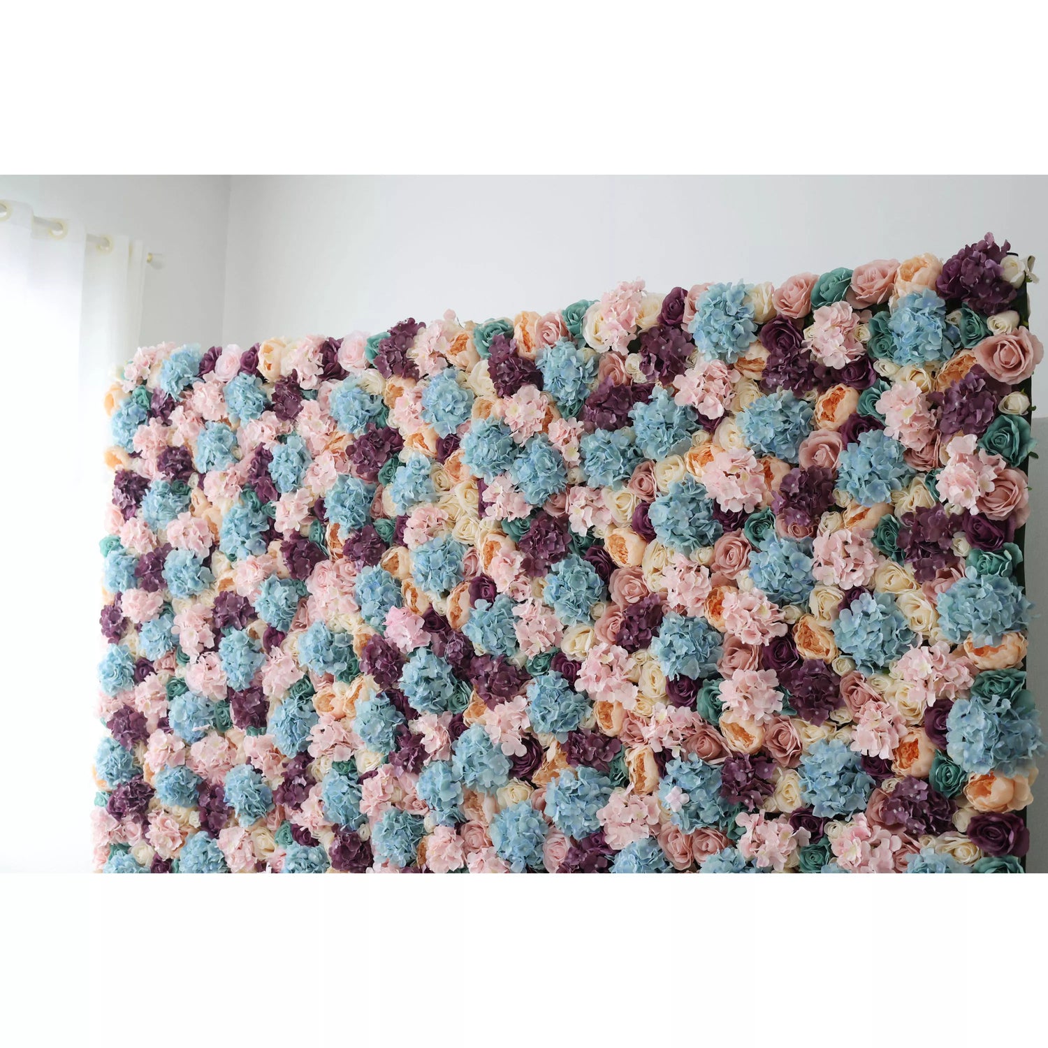 This is a large artificial flower wall, a vibrant tapestry of pastel hues—soft pinks, blues, purples, and creams. Densely packed with varied blooms like hydrangeas and roses, it creates a lush, textured display. Perfect for event backdrops, adding an elegant, colorful touch to weddings or parties, enhancing the decorative appeal of any space.