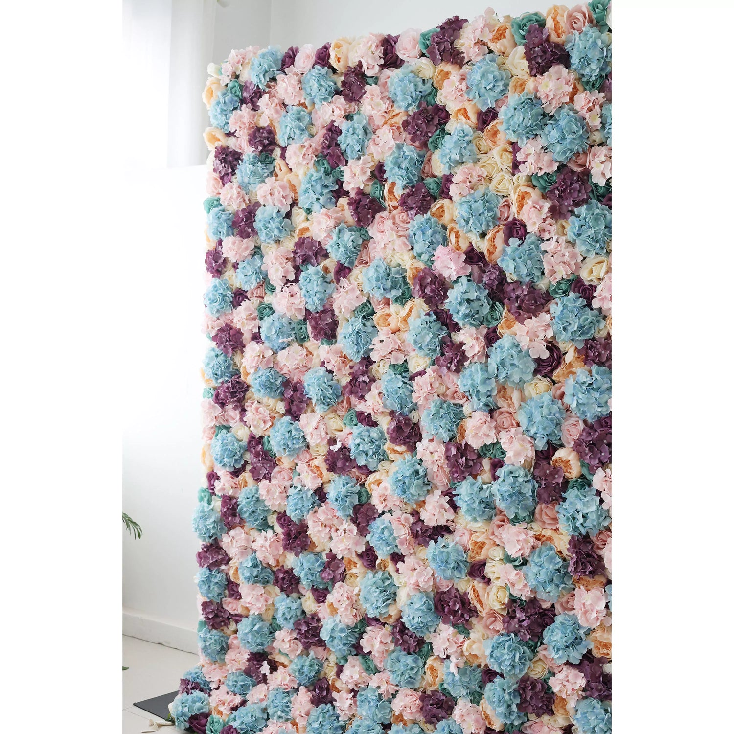 This large artificial flower wall is a vibrant tapestry of pastel hues—soft pinks, blues, purples, and creams. Densely packed with diverse blooms like hydrangeas and roses, it creates a lush, textured display. Ideal for event backdrops, it adds an elegant, colorful touch to weddings or parties, enhancing the decorative appeal of any space.