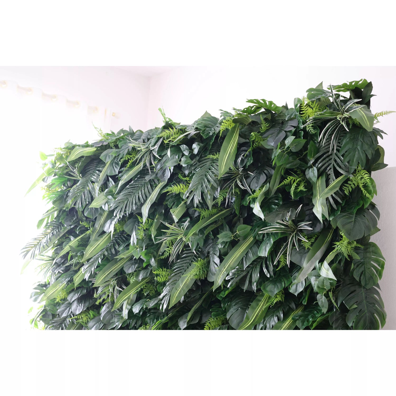 This picture shows a large, lush artificial greenery wall. It’s densely packed with various green leaves—like ferns, palm - like fronds, and other tropical - looking foliage. The rich, verdant arrangement creates a natural, jungle - inspired vibe. Placed against a bright, plain background, it adds a touch of nature to the space, perfect for decorative uses in events or interiors, bringing an instant fresh and lively feel.