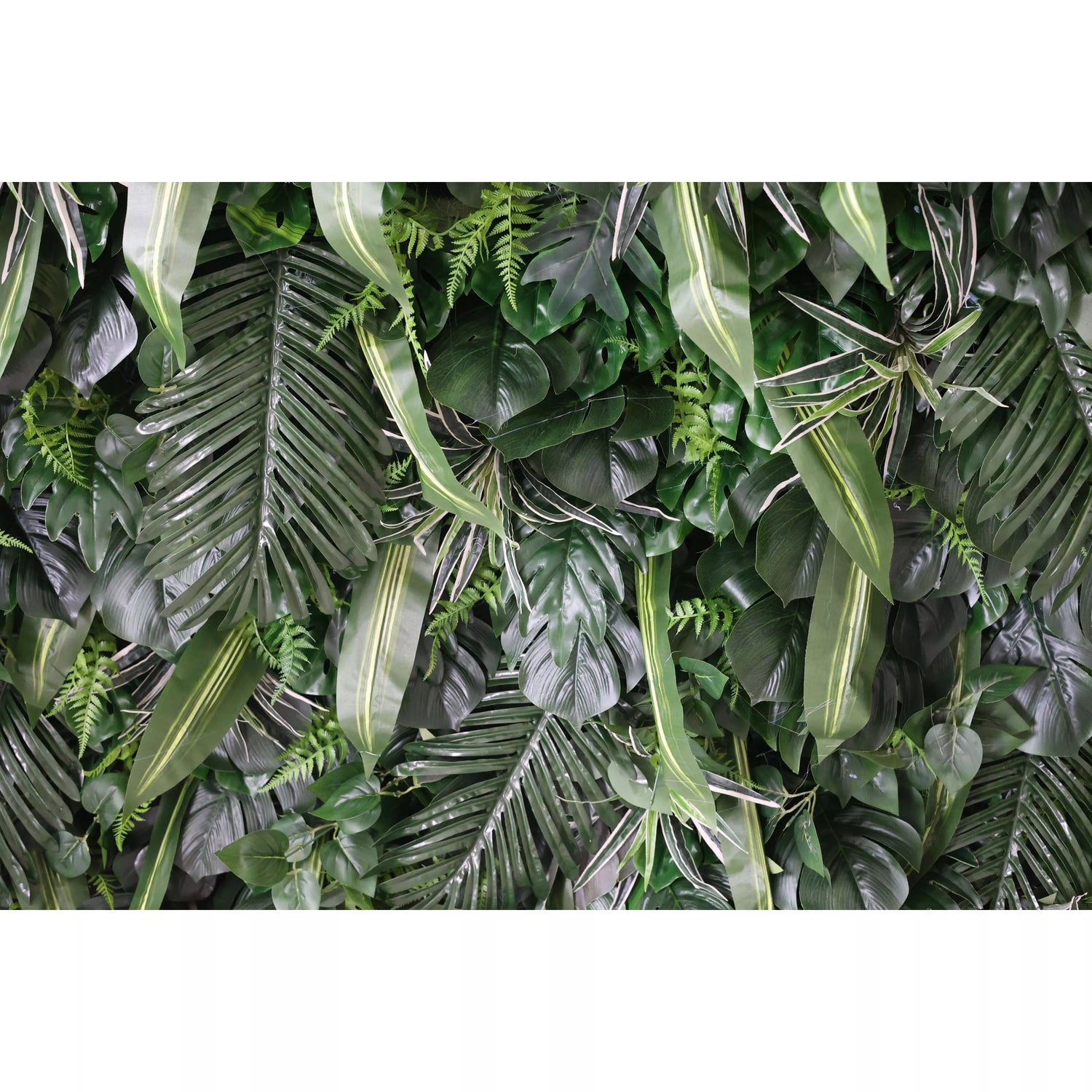 This is a close - up of a lush artificial greenery wall. It features a dense mix of tropical - looking leaves, including palm fronds, ferns, and broad - bladed plants. The varied shapes, textures, and shades of green create a vibrant, natural - looking display. Ideal for adding a touch of nature to indoor spaces, like event backdrops or interior decor, bringing a fresh, lively ambiance.
