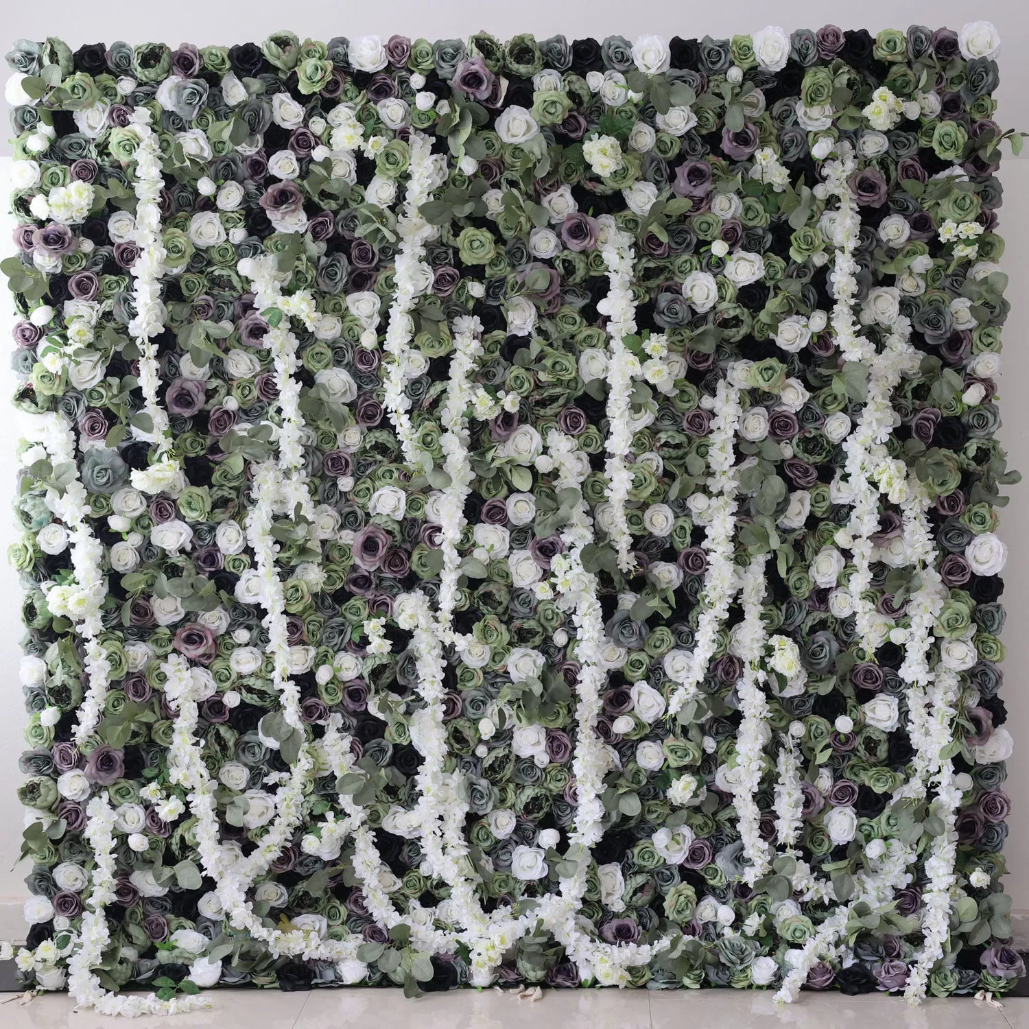 This is a large artificial flower wall with a green - dominated color scheme. It features white blossoms, purple roses, and dense green foliage. The arrangement includes cascading white floral vines, creating a lush, natural - looking display. Ideal for decorative event backdrops, adding an elegant and verdant touch.