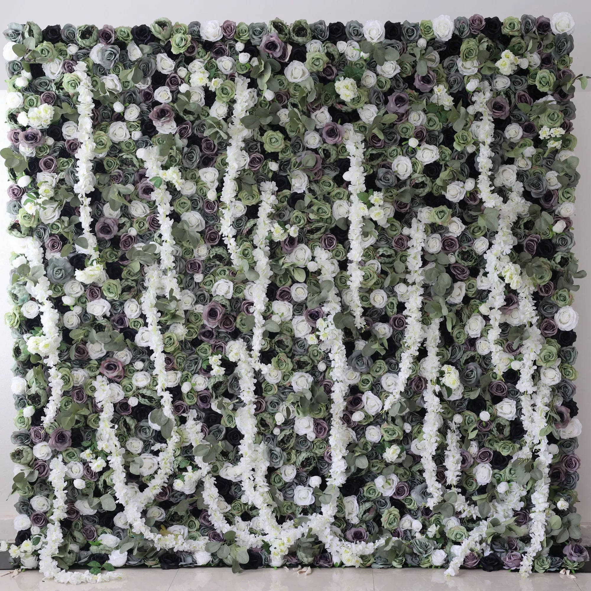 This is a large artificial flower wall with a green - dominated color scheme. It features white blossoms, purple roses, and dense green foliage. The arrangement includes cascading white floral vines, creating a lush, natural - looking display. Ideal for decorative event backdrops, adding an elegant and verdant touch.