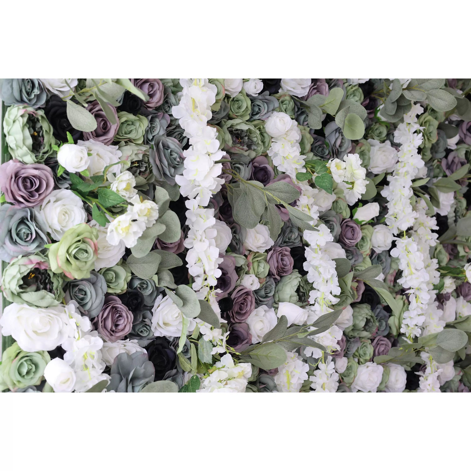 This close - up shows a lush artificial flower wall. It has a mix of white, green, and purple roses, plus white blossoms and green leaves. The dense, textured arrangement creates an elegant, natural - looking display, perfect for decorative backdrops at events like weddings.