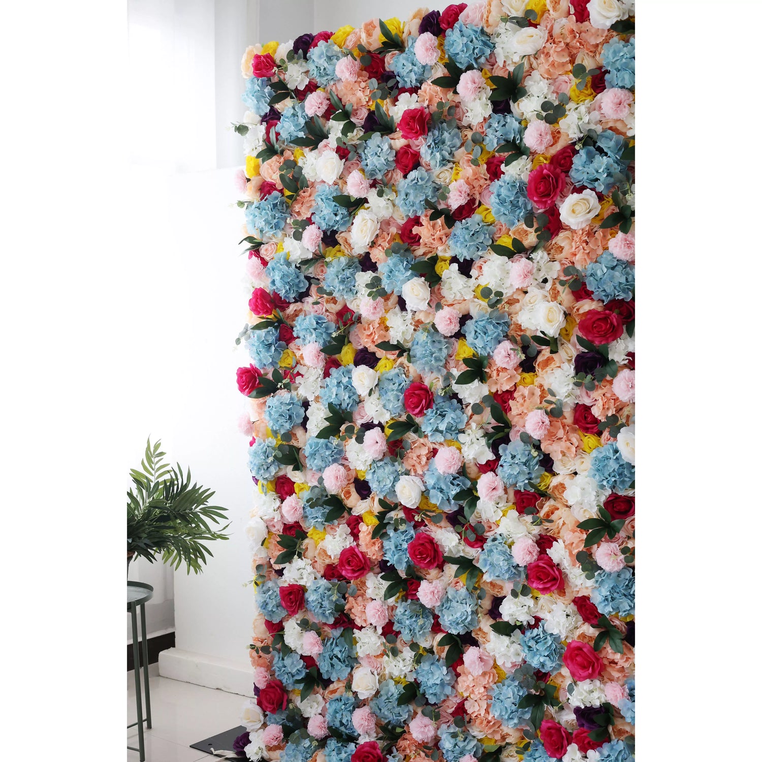 This is a large, vibrant artificial flower wall. It features a dense mix of colorful blooms—blue hydrangeas, pink roses, white flowers, and yellow blossoms. The lush arrangement creates a lively, eye - catching display, perfect for event backdrops, adding a cheerful and decorative touch to the space.