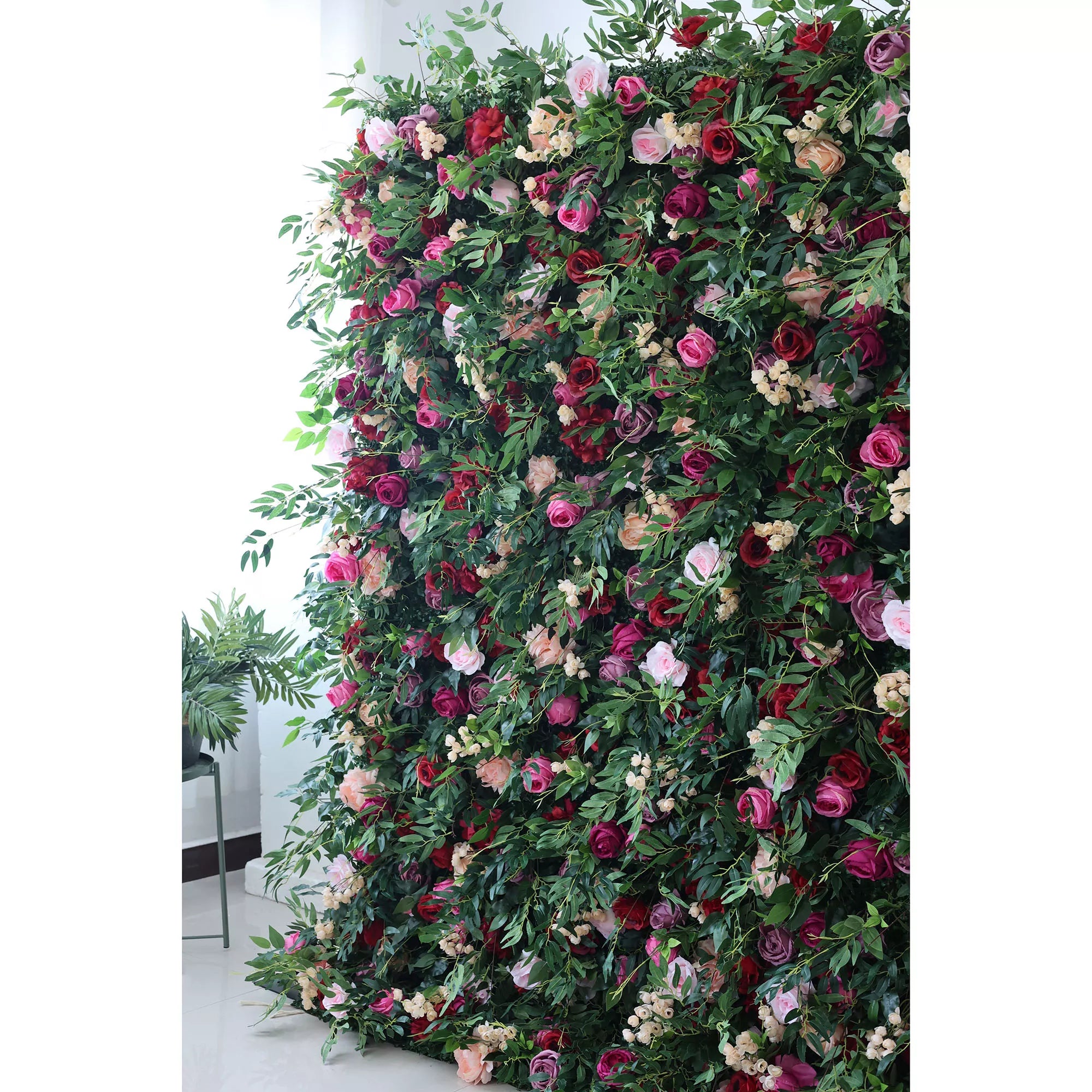 A lush artificial flower wall bursts with color—pink, red, purple roses, soft peach blooms, and delicate white flowers—all woven through green foliage. It creates a romantic, natural - looking backdrop, perfect for events or adding elegance to a space.