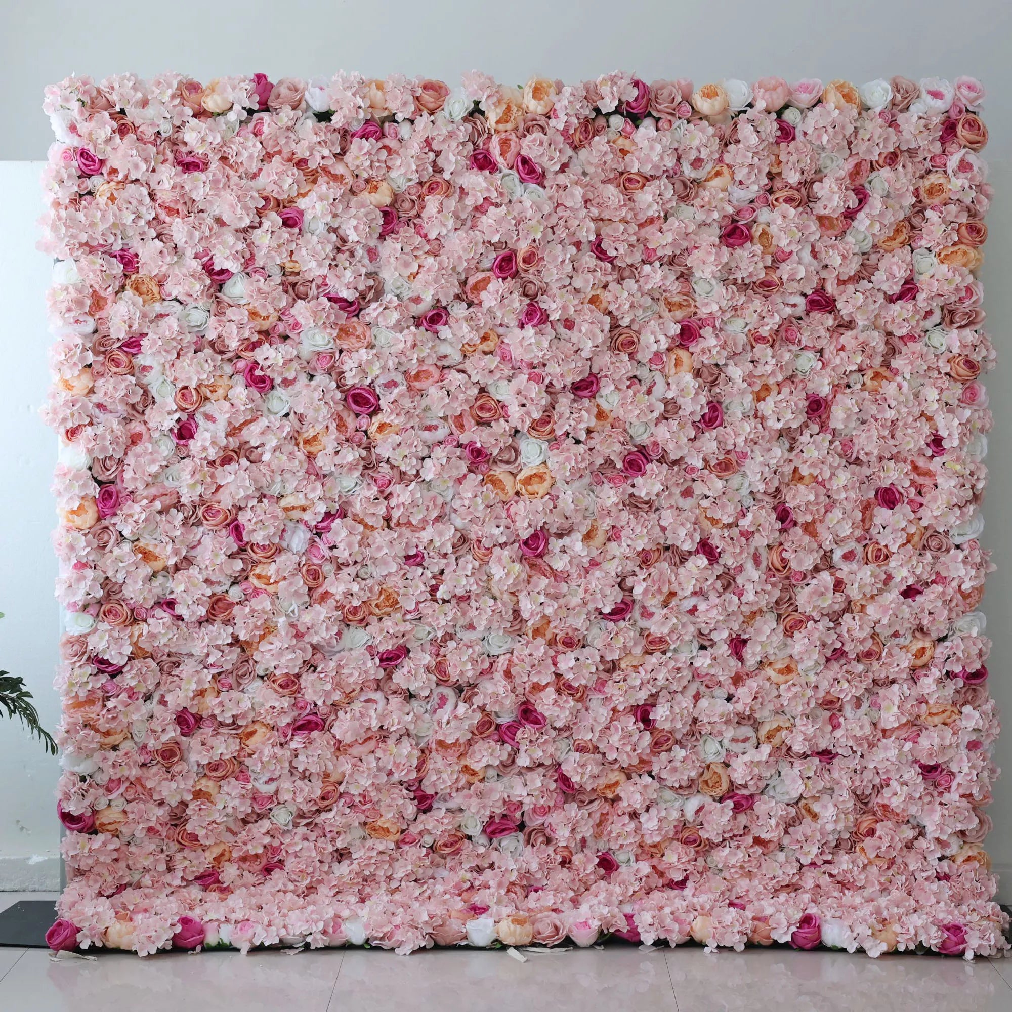 This flower wall is a lush, romantic display of artificial blooms. A soft pink base, dotted with peach - colored roses, deeper pink blossoms, and white flowers, creates a dreamy, textured pattern. The dense arrangement and gentle color palette make it perfect for weddings or elegant events, exuding charm and warmth.