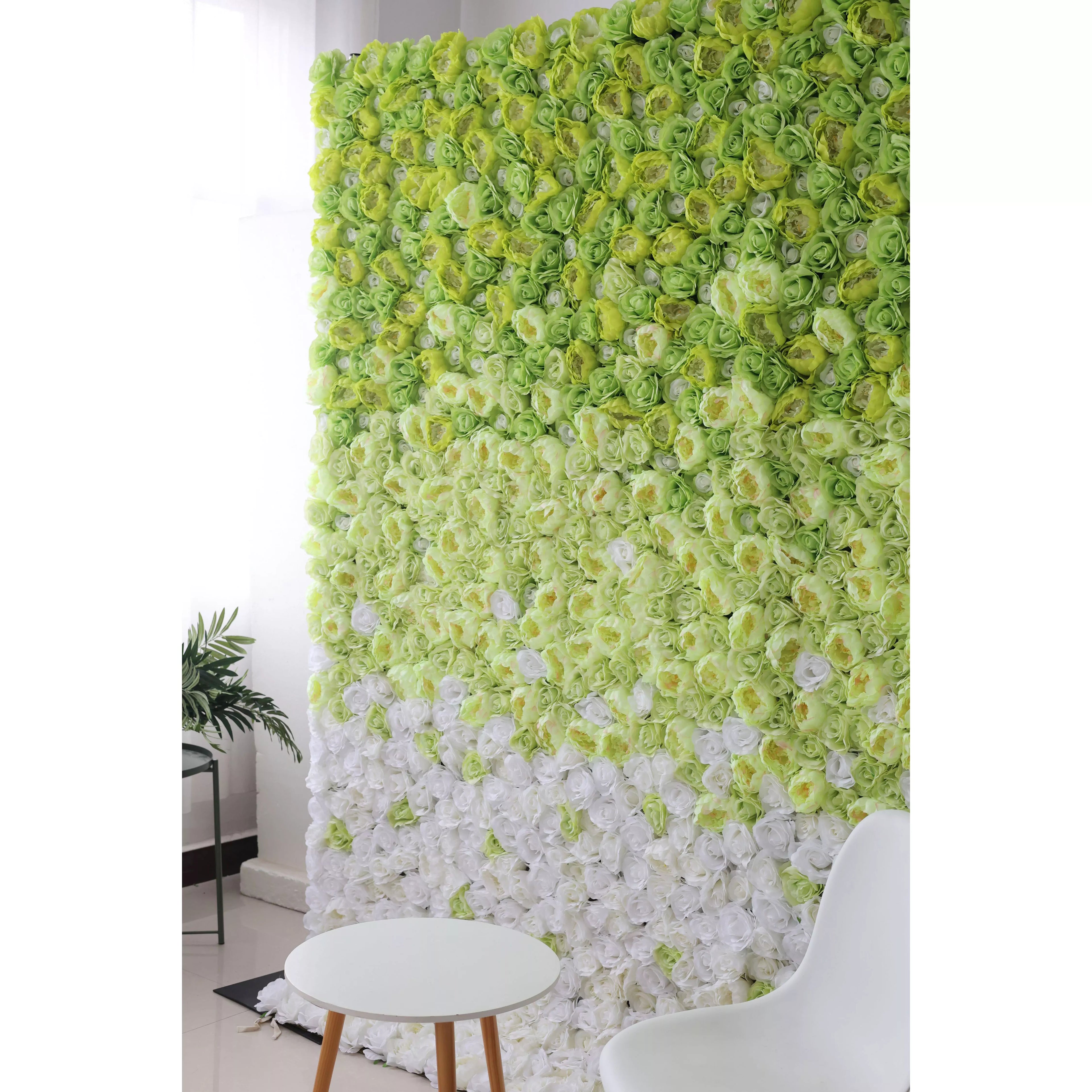 This flower wall showcases a stunning gradient of artificial roses, transitioning from vibrant green at the top to pure white at the bottom. The dense arrangement creates a lush, textured backdrop. Complemented by a minimalist white table and chair, it exudes a fresh, elegant charm, perfect for photo ops or event decor.