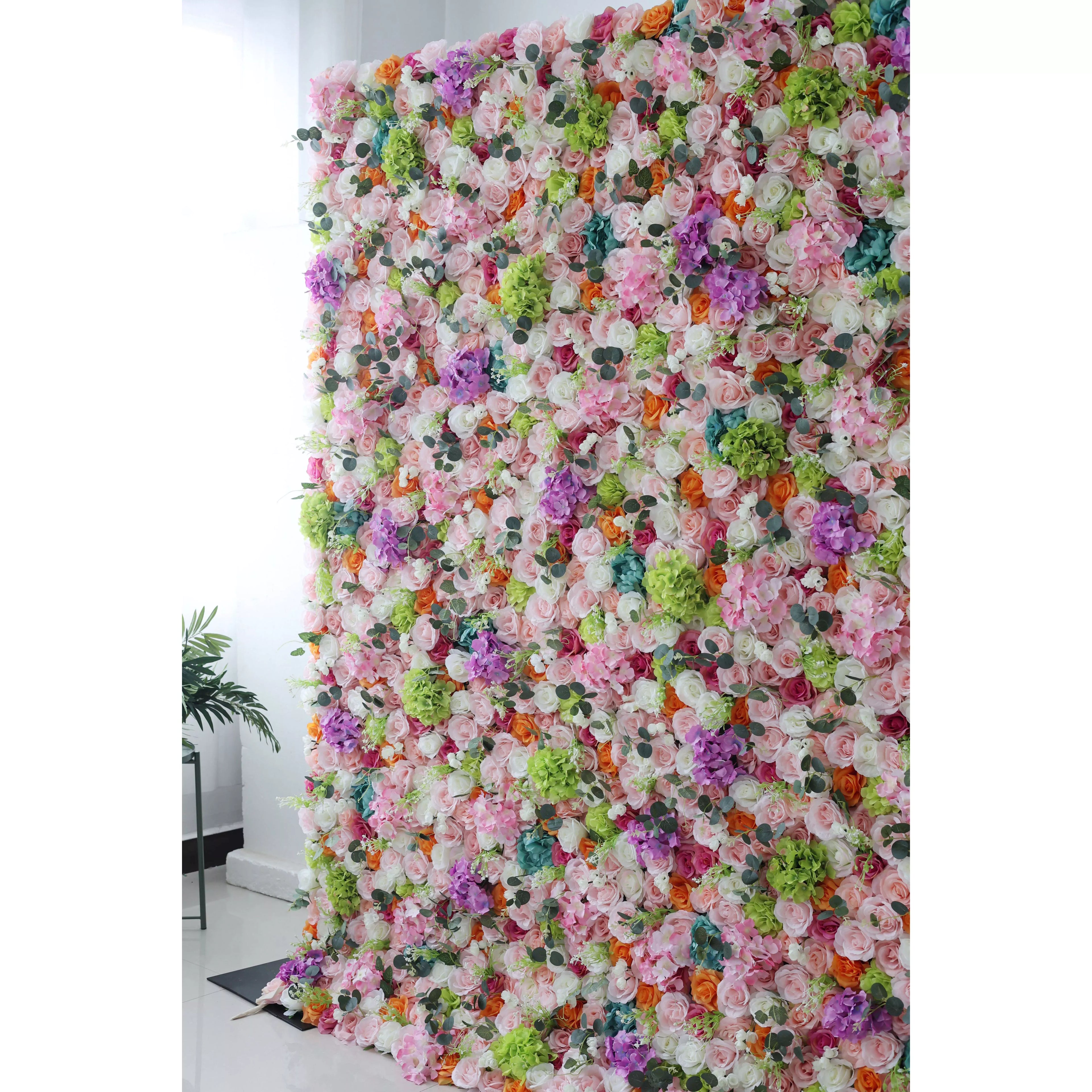 This flower wall is a vibrant, dense arrangement of artificial flowers. It features a diverse color palette—white, pink, purple, orange, green, and blue—with various blooms like roses and hydrangeas. Ideal for events, it creates a lively, celebratory atmosphere, adding charm to backdrops for photos or ceremonies.