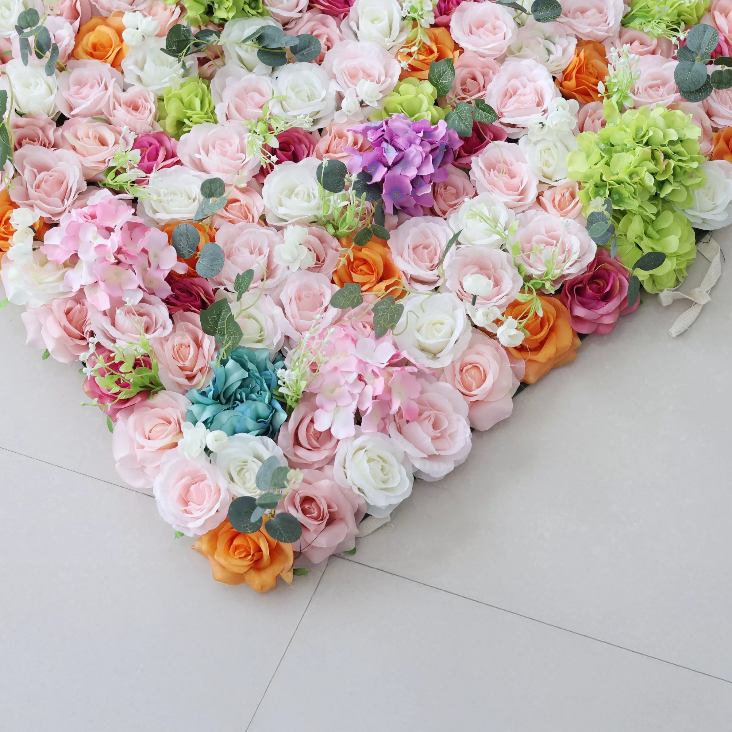 This is a close-up of a vibrant artificial floral arrangement from **Valar Flowers**, featuring a lush mix of soft pink, white, orange, deep red, purple, and turquoise blooms, complemented by green hydrangeas and eucalyptus leaves. Densely packed and layered, it creates a romantic, elegant aesthetic ideal for wedding decor, photo backdrops, or special event styling.