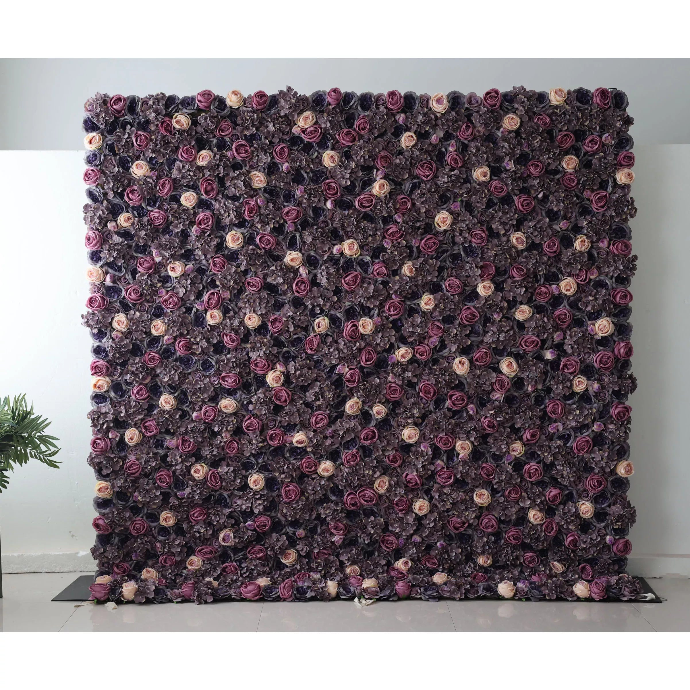 This flower wall is a dense, elegant arrangement of artificial blooms. A rich palette of deep purple, lavender, and soft peach roses, paired with dark hydrangeas, creates a sophisticated, romantic texture. The uniform layout and moody hues make it perfect for upscale events like weddings, exuding a sense of luxury and charm.