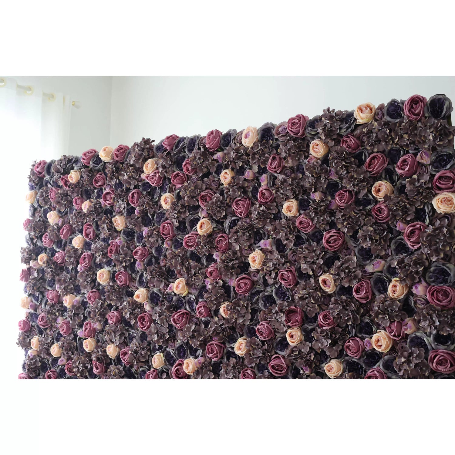 This flower wall is a lush, elegant display of artificial blooms. Deep purple, lavender, and soft peach roses are interspersed with dark hydrangeas, creating a rich, textured pattern. The dense arrangement and moody color palette exude sophistication, making it ideal for upscale events like weddings, adding a touch of luxury and romance.