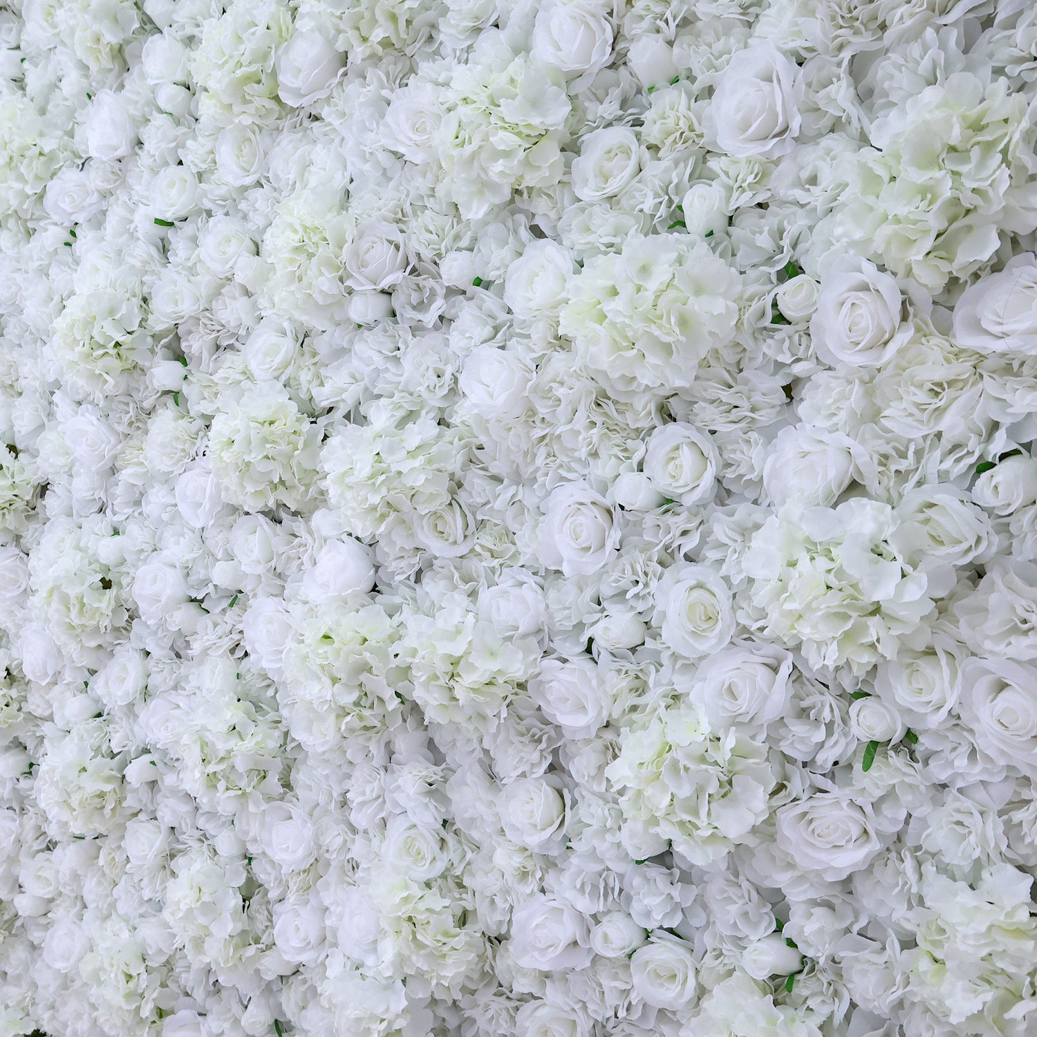 A dense arrangement of artificial white flowers forms a lush wall. It features various blooms like roses and hydrangeas, with subtle green leaves peeking through. The pure white hues create an elegant, romantic look, perfect for events such as weddings, bridal showers, or upscale parties needing a sophisticated backdrop.