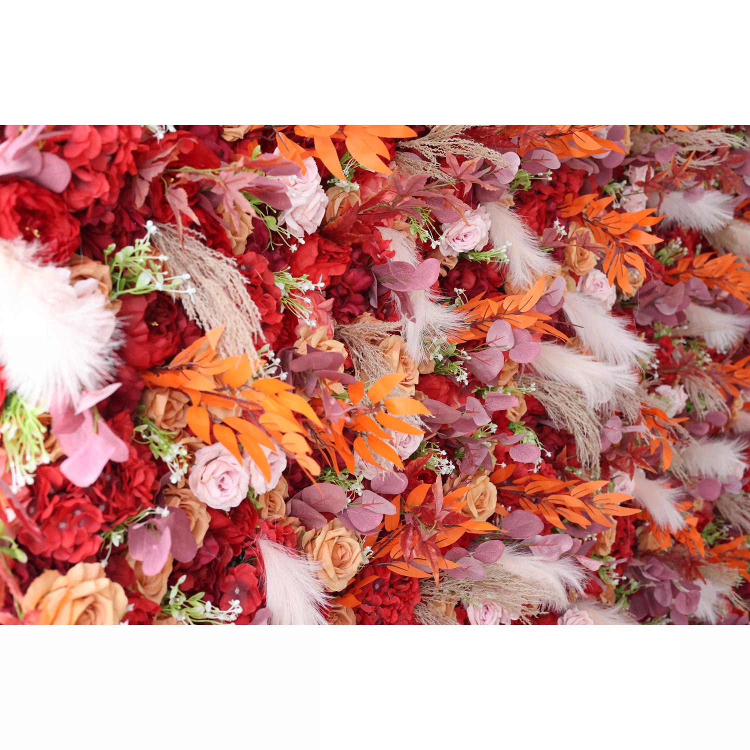 This flower wall is a lush arrangement of artificial flowers. It features a rich color palette with deep red blossoms, peach - colored roses, and orange leaves, along with white fluffy pampas grass and purple foliage. Ideal for decorative backdrops at events like weddings, adding a warm and romantic ambiance.