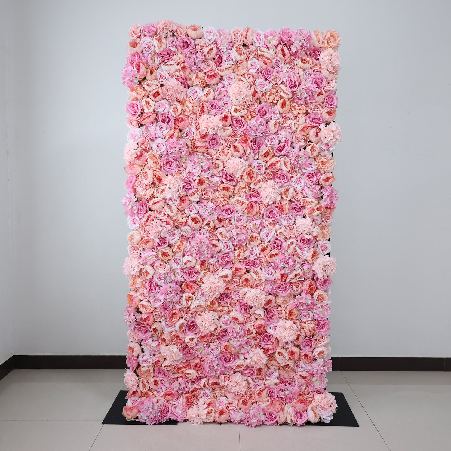 This image showcases a stunning pink floral backdrop by ValarFlowers, set indoors. It features a dense arrangement of artificial flowers in various shades of pink, creating a lush, textured display. The elegant design exudes sophistication, perfect for adding a luxurious, nature-inspired element to events or interiors.