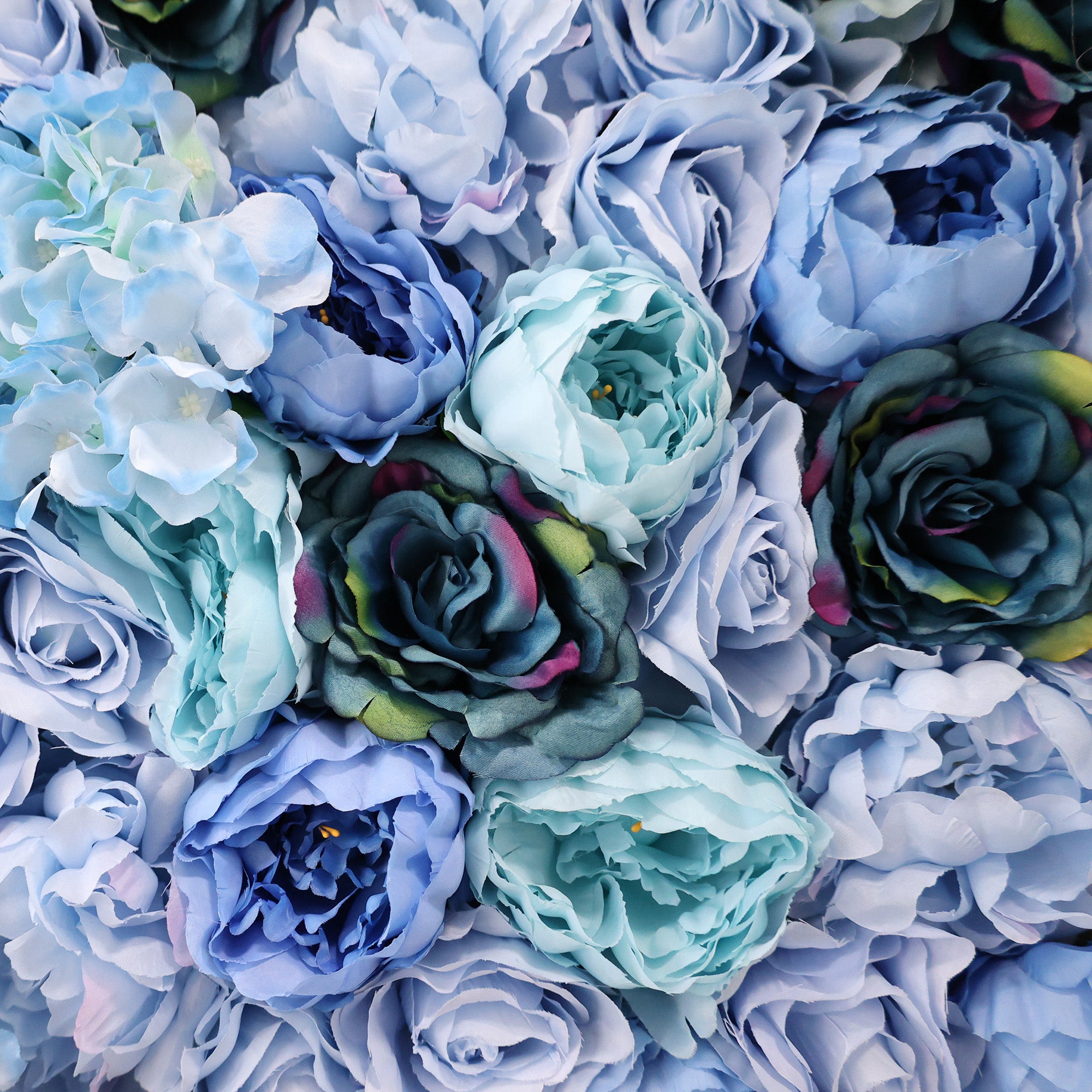 This image showcases a dense arrangement of artificial flowers in various shades of blue, including roses, peonies, and hydrangeas. The textured petals range from light sky blue to deep navy, with some blooms featuring subtle hints of pink and green, creating a lush, elegant display ideal for a luxurious, nature-inspired backdrop.