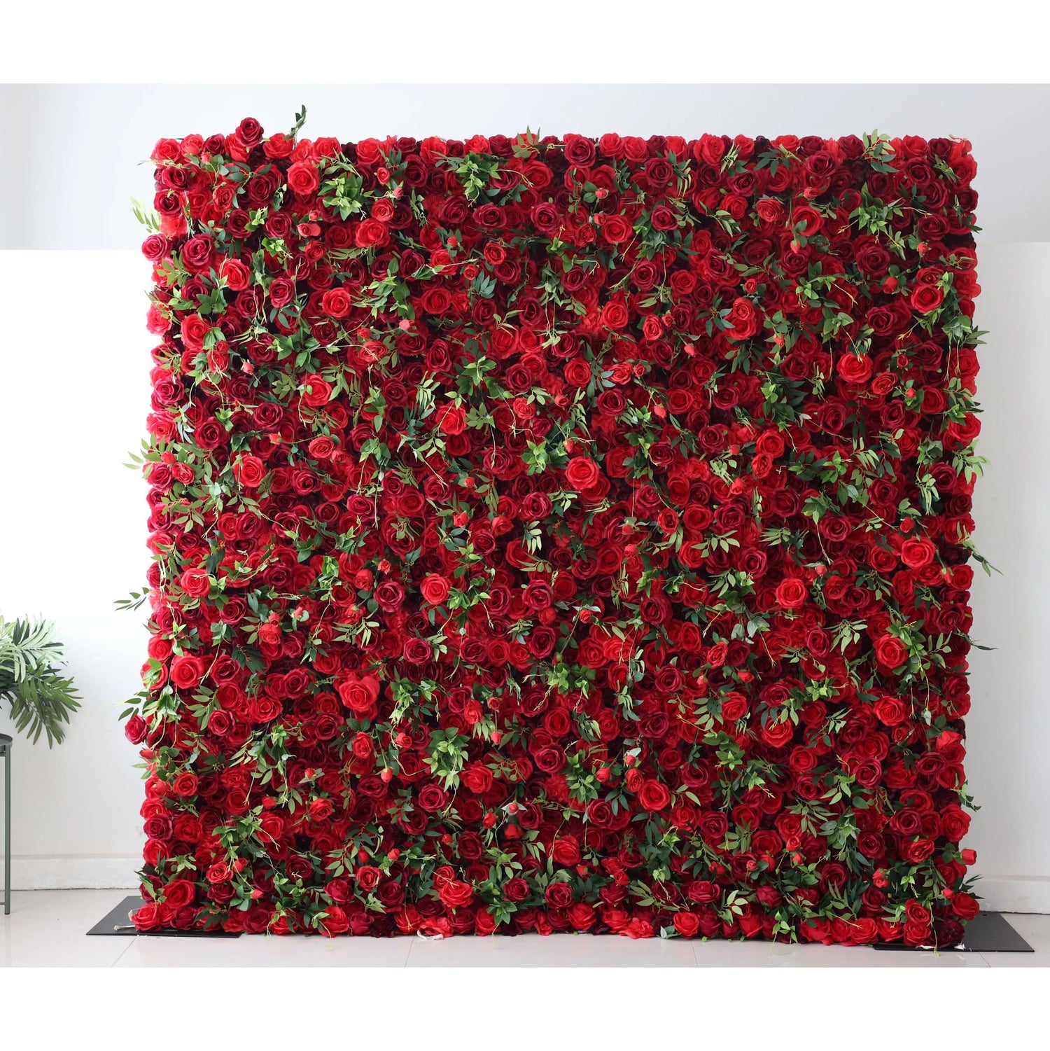 This flower wall is a grand display of artificial red roses, densely packed with lush green leaves. The vibrant red blooms create a passionate, romantic texture, while the greenery adds freshness. Perfect for weddings or events, it exudes elegance and intensity, serving as a captivating backdrop for photos and decor.