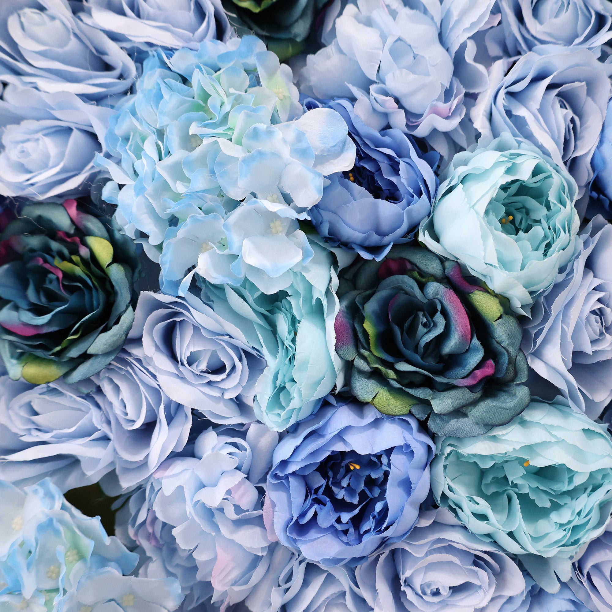 This image showcases a dense arrangement of artificial flowers in various shades of blue—from light sky blue to deep navy. Featuring roses, hydrangeas, and peonies, the textured display exudes elegance, ideal for a luxurious, nature-inspired backdrop, likely by ValarFlowers, perfect for events or interiors.