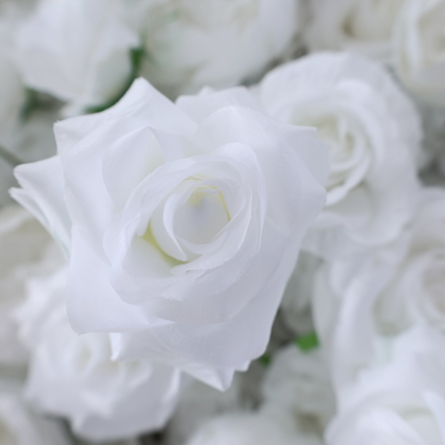 This picture features a close - up of a white artificial rose. The petals are soft and smooth, with a pristine white hue that gives a sense of purity. The rose's layers of petals are neatly arranged, creating a delicate and elegant appearance. Surrounding it are other similar white artificial roses, forming a lush cluster. The overall scene exudes a serene and sophisticated charm, ideal for decorative purposes in events or as part of a floral arrangement, evoking feelings of beauty and refinement.