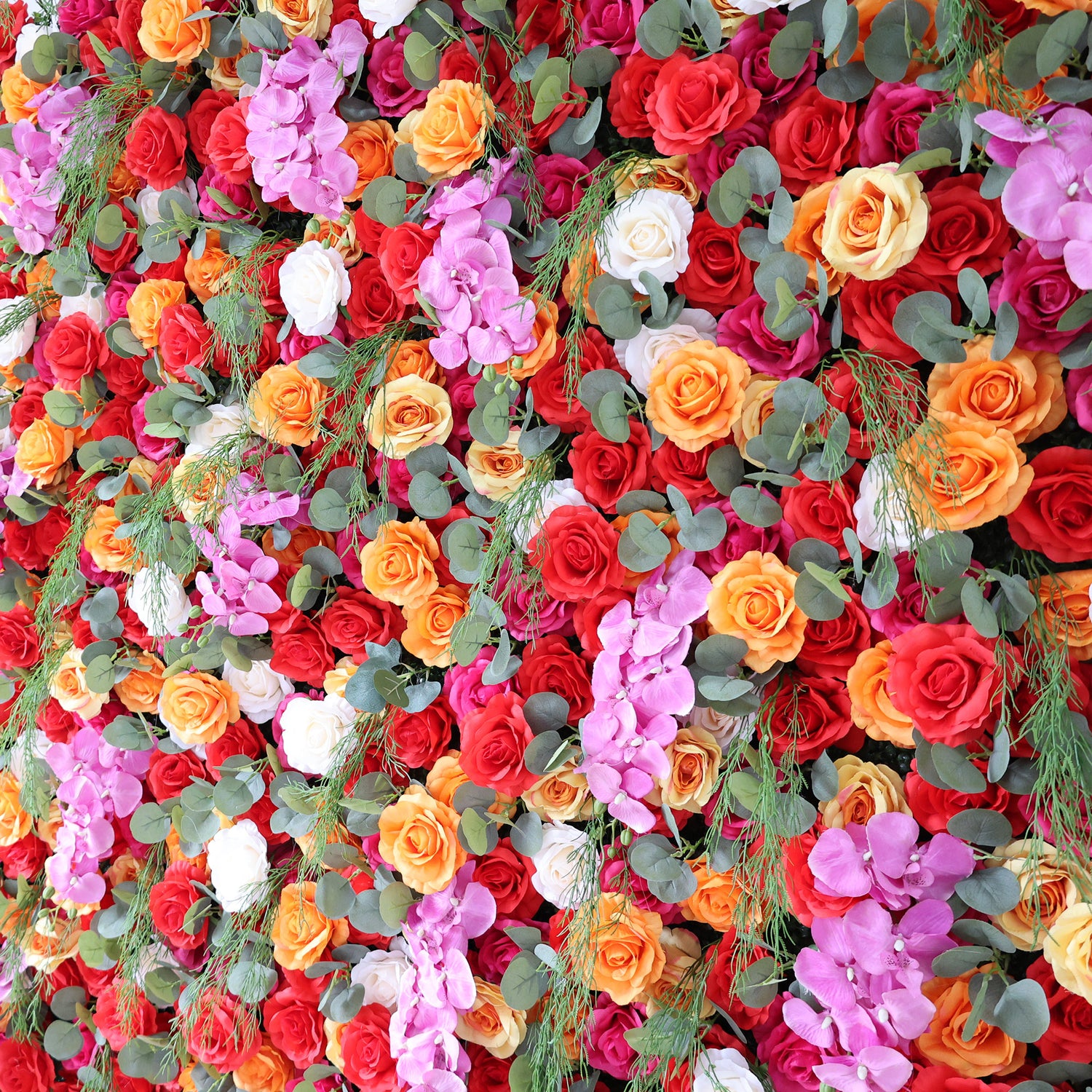 This image showcases a vibrant floral arrangement by Valar Flowers. It features a dense cluster of artificial flowers in a rich palette of red, orange, pink, and white, including roses and other complementary blooms, interspersed with lush green foliage. The flowers are intricately arranged to create a lush, textured, and visually striking display. Perfect for adding a touch of energy and elegance to events or spaces, the arrangement exudes a lively and sophisticated atmosphere.