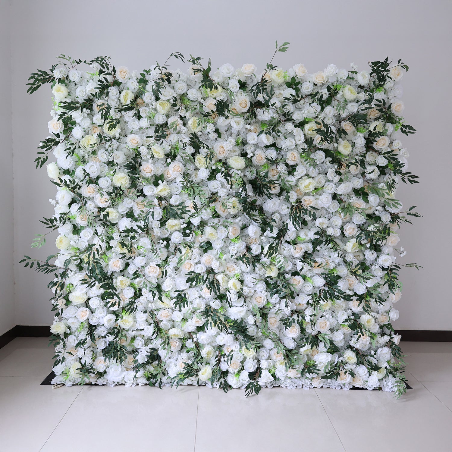 This image showcases a stunning floral wall by Valar Flowers. It features a dense arrangement of artificial flowers in soft shades of white and cream, interspersed with lush green foliage. The meticulously crafted blooms create a lush, elegant, and visually soothing display. Perfect for adding a touch of timeless beauty to events or spaces, this floral wall exudes a refined and sophisticated atmosphere.