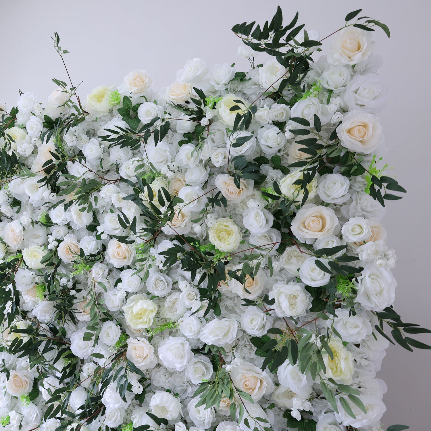 This image showcases a stunning floral arrangement by Valar Flowers. It features a dense cluster of artificial flowers in soft shades of white and cream, interspersed with lush green foliage. The meticulously crafted blooms, including roses and other complementary flowers, create a lush, elegant, and visually soothing display. Perfect for adding a touch of timeless beauty to events or spaces, this arrangement exudes a refined and sophisticated atmosphere.
