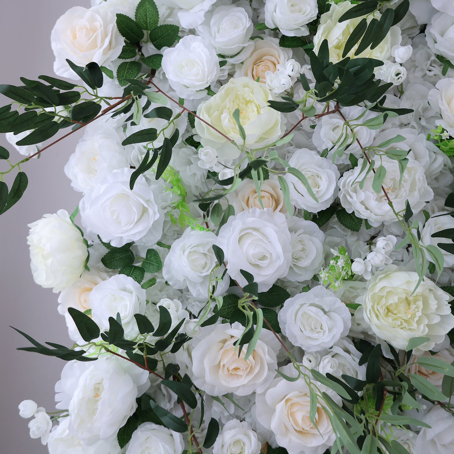 This image showcases a stunning floral arrangement by Valar Flowers. It features a dense cluster of artificial flowers in soft shades of white and cream, interspersed with lush green foliage. The meticulously crafted blooms, including roses and other complementary flowers, create a lush, elegant, and visually soothing display. Perfect for adding a touch of timeless beauty to events or spaces, this arrangement exudes a refined and sophisticated atmosphere.