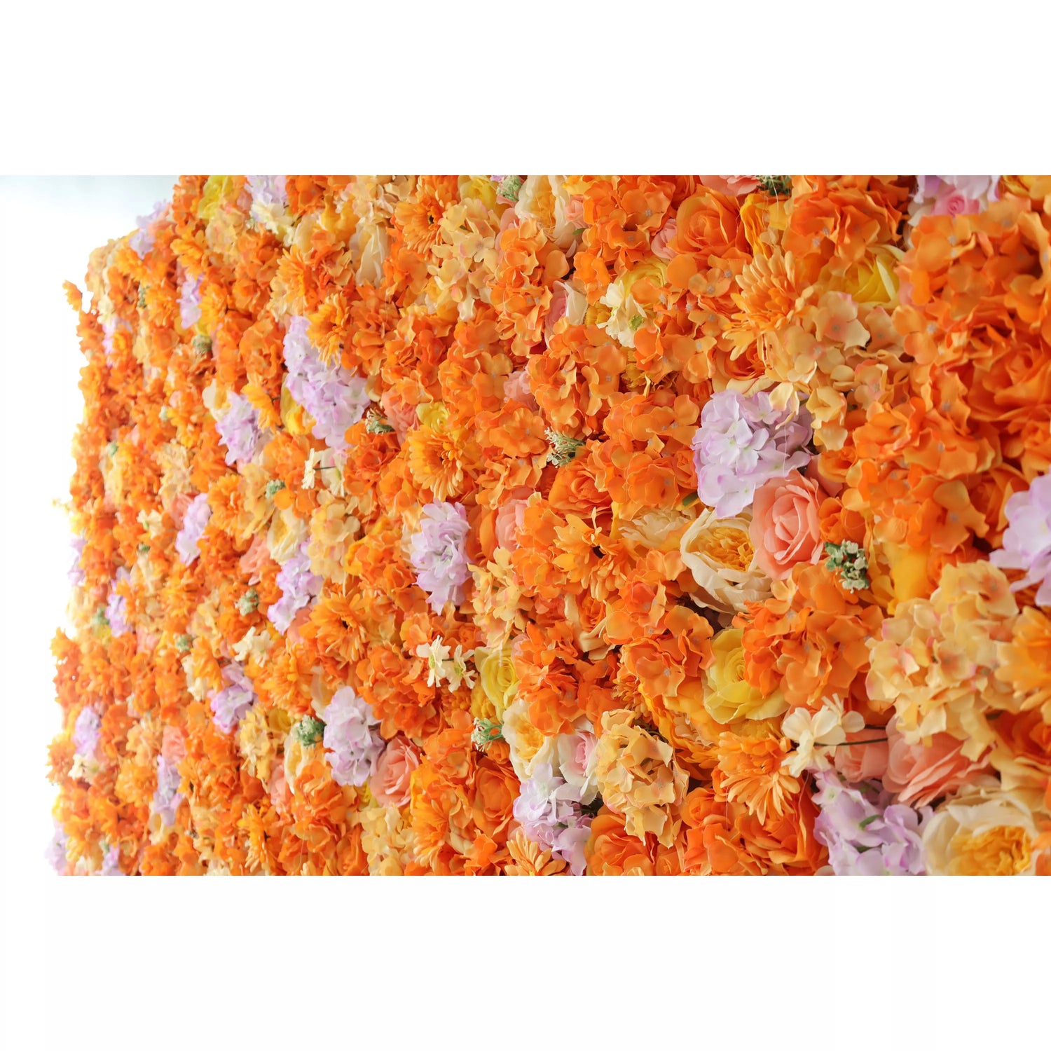 This image showcases a vibrant floral wall by Valar Flowers. Densely packed with artificial flowers, it features a rich palette of warm oranges, complemented by soft purples and creamy hues. The flowers, including roses and other blooms, create a lush, colorful, and visually striking display, exuding an elegant and lively charm, perfect for decorative use in events or as a stunning interior accent.