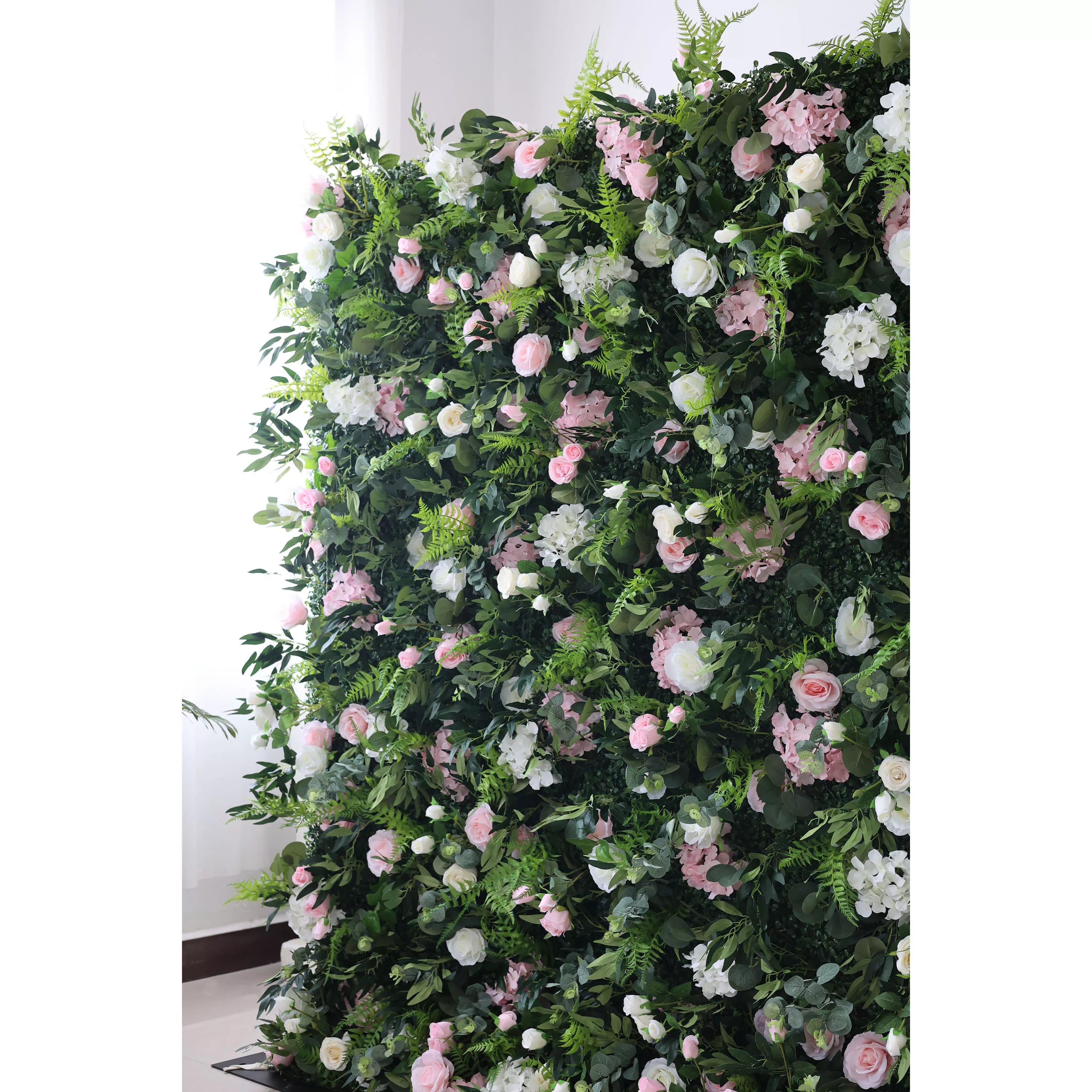 This lush, cascading floral wall is a dense tapestry of deep green foliage, interwoven with blush pink roses, soft white blooms, and delicate filler flowers. The layered, organic design creates a rich, three-dimensional texture, evoking a fresh, romantic, and naturally elegant atmosphere—ideal for weddings, photo backdrops, or elegant indoor celebrations.