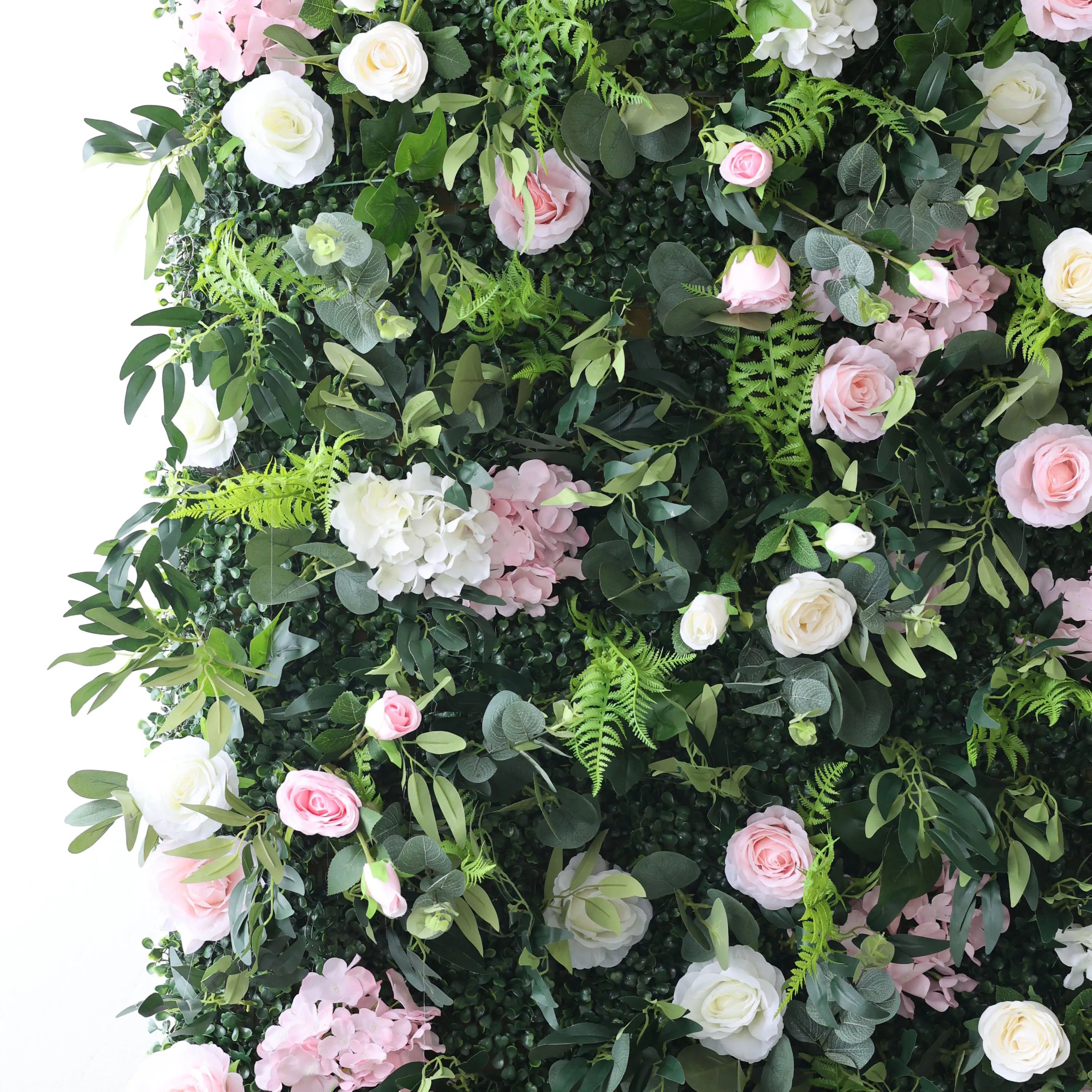 This close-up captures a lush floral wall with a dense, textured backdrop of deep green foliage, including ferns and eucalyptus leaves. It is interspersed with a romantic mix of blush pink roses, soft white roses, and pink-and-white hydrangeas. The layered, organic design creates a rich, three-dimensional texture, evoking a fresh, natural, and romantic atmosphere ideal for weddings, photo backdrops, or elegant celebrations.