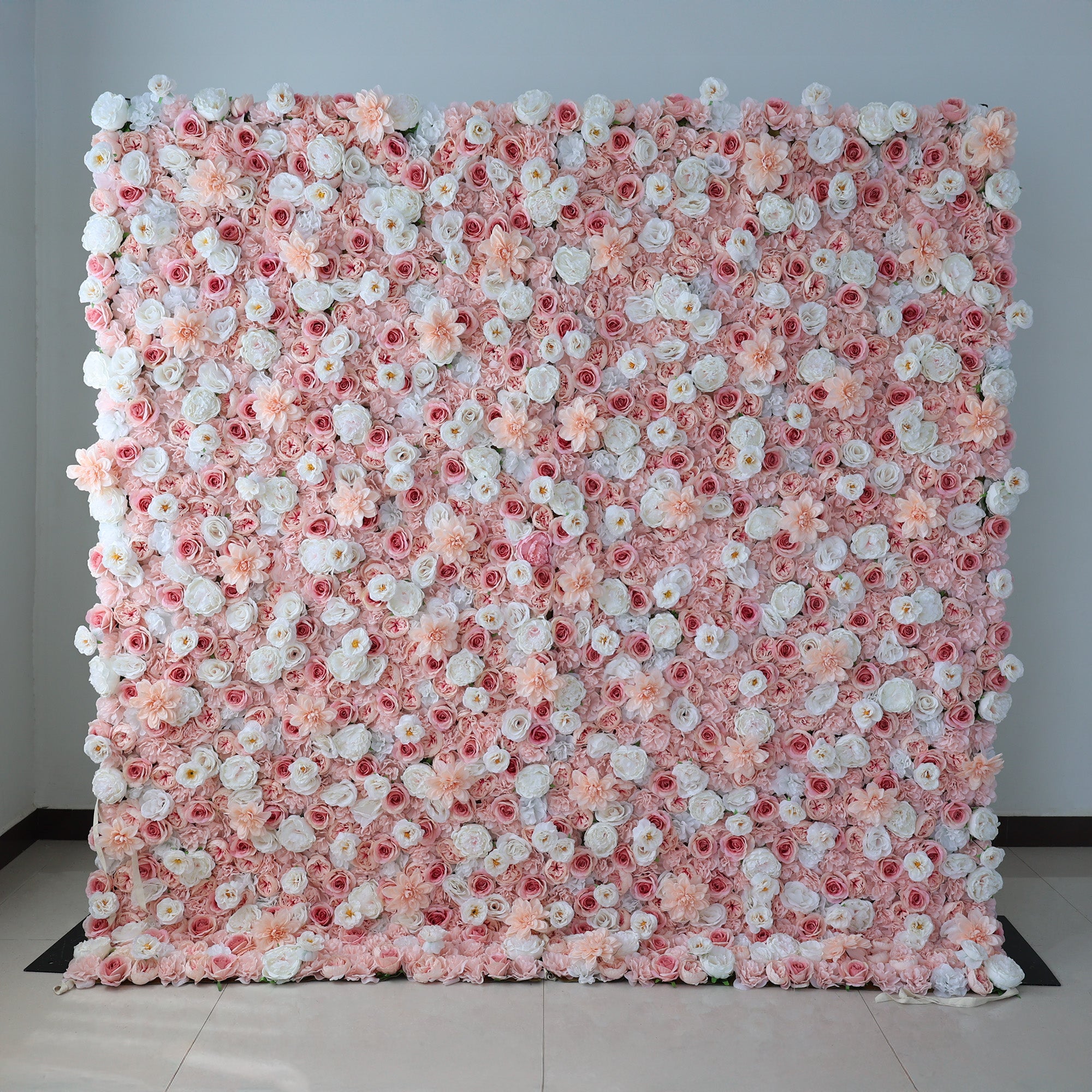 A large, square floral wall showcases a vibrant mix of pink, blush, and white artificial flowers. Dense clusters of roses, peonies, and smaller blooms create a lush, romantic display. Set against a plain light - colored wall with a tiled floor, it exudes elegance, perfect for weddings, photo backdrops, or upscale events needing a charming, floral focal point.
