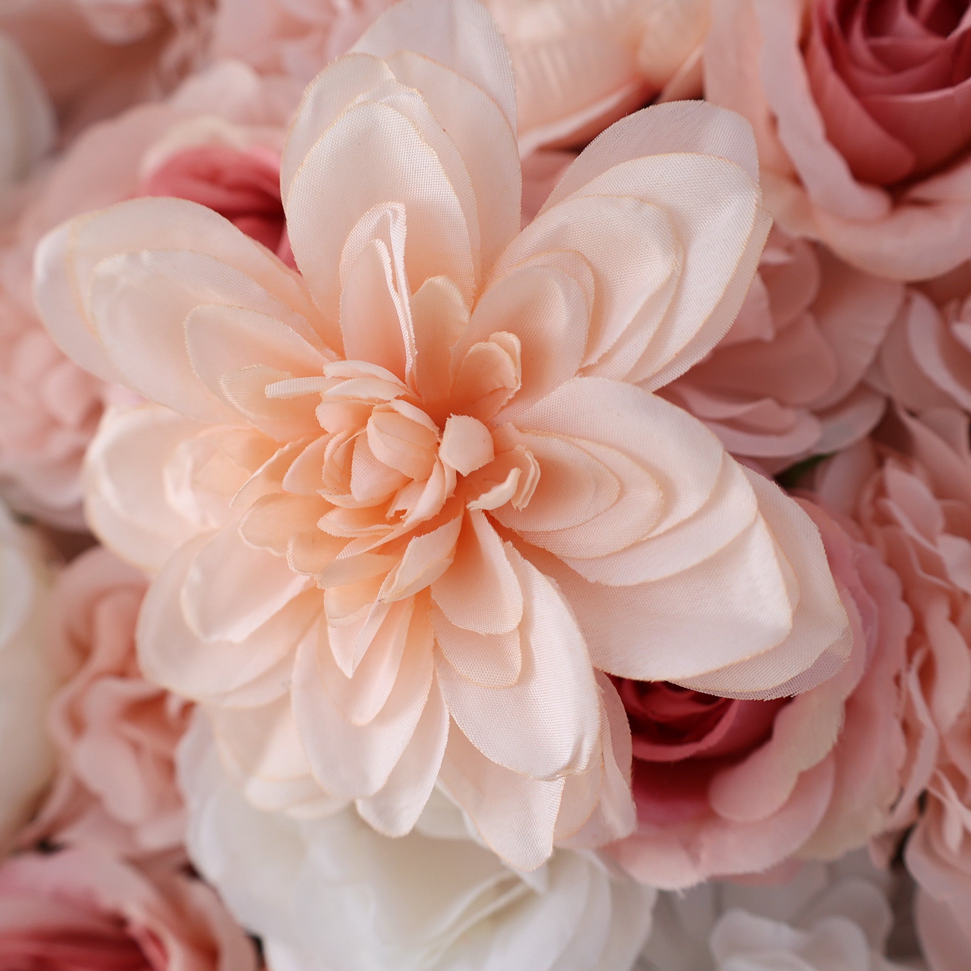 A close - up of an artificial peach - colored flower with layered petals takes center stage. Surrounding it are other faux flowers in shades of pink and white. The petals have a smooth, slightly shiny texture, giving the flower a delicate and realistic appearance, ideal for decorative floral arrangements.