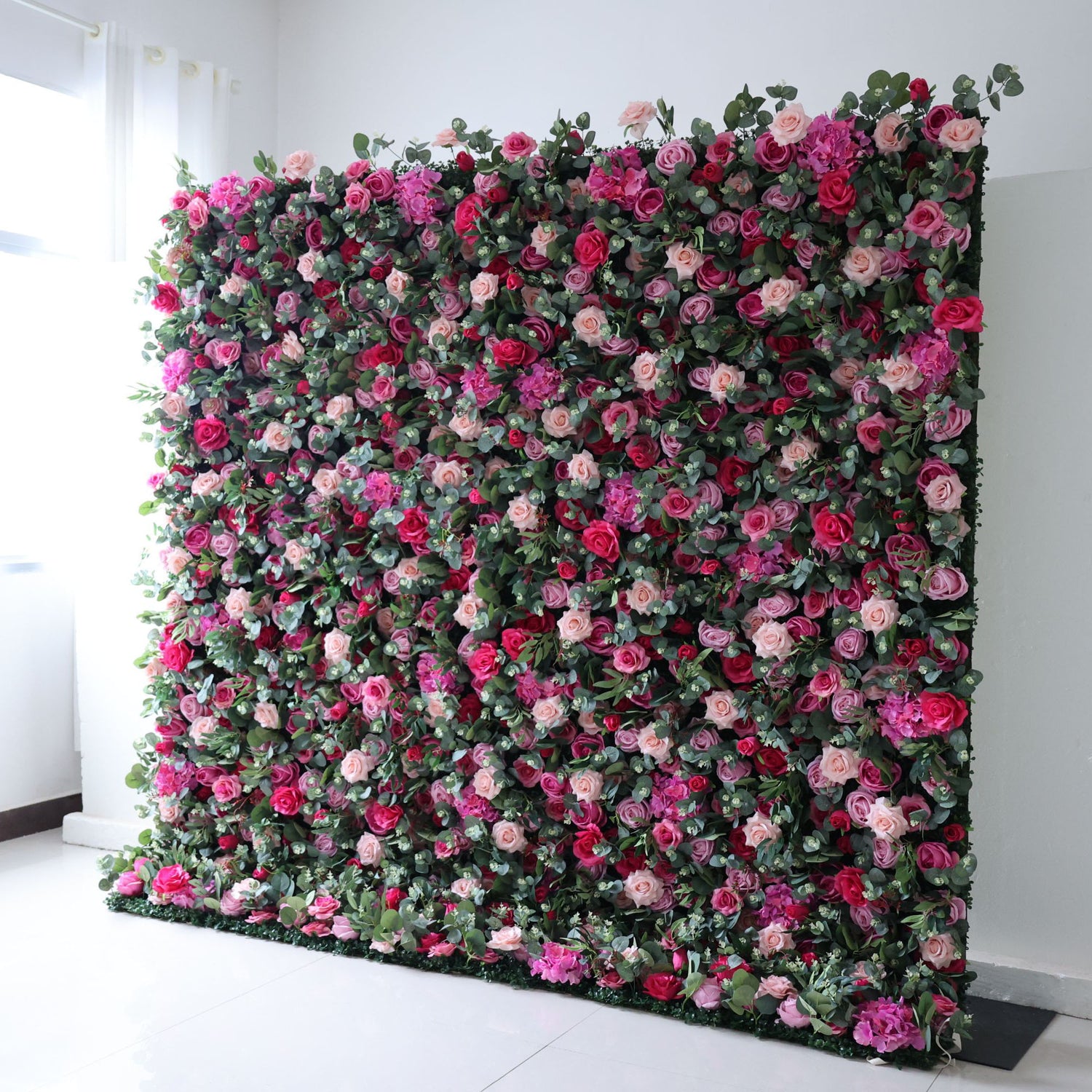 The arrangement features a beautiful combination of pink and white flowers. The flowers are meticulously arranged in an organized manner, creating an eye-catching display. The wall is adorned with various types of flowers, including roses, lilies, and other blooms, strategically placed to create a visually appealing design.