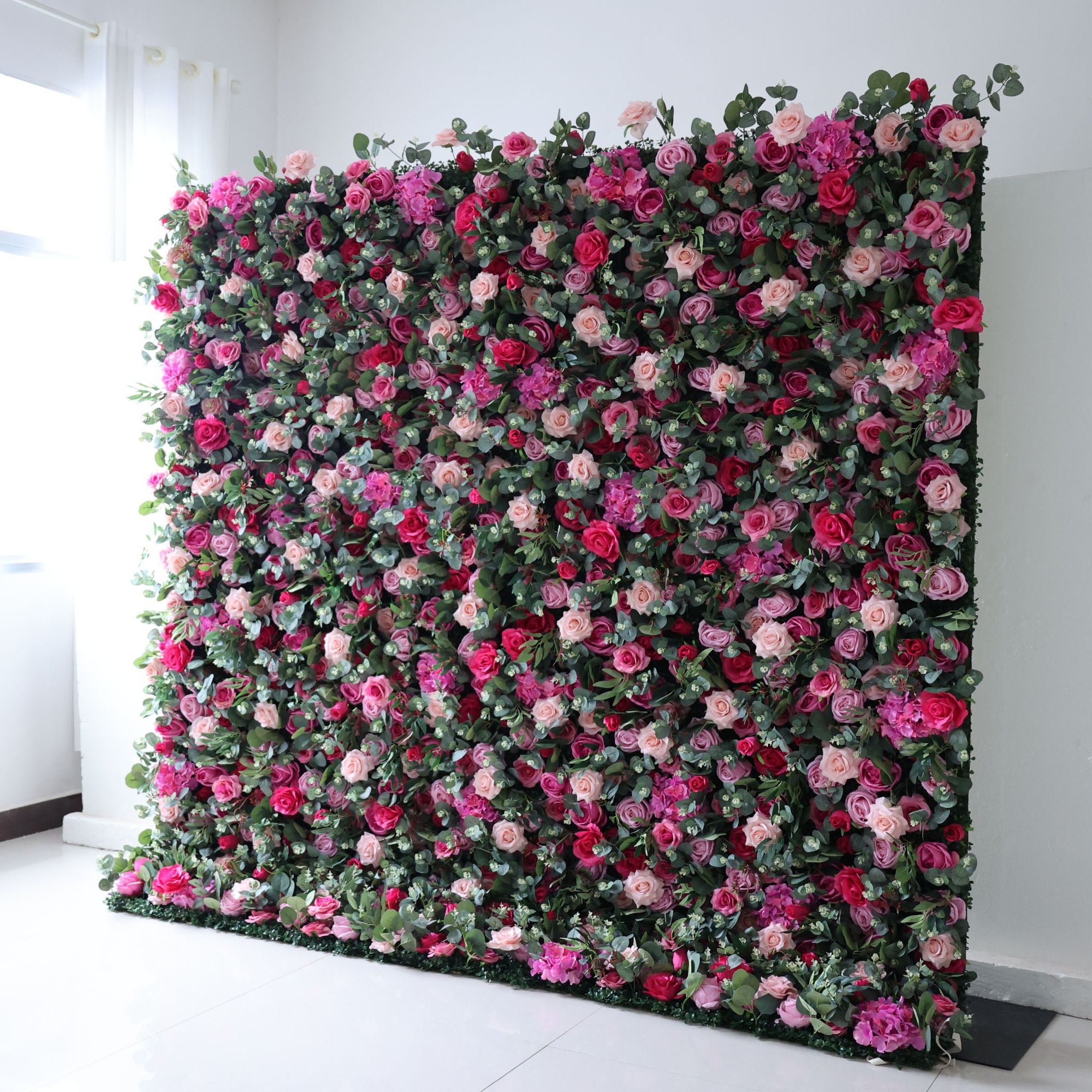 The arrangement features a beautiful combination of pink and white flowers. The flowers are meticulously arranged in an organized manner, creating an eye-catching display. The wall is adorned with various types of flowers, including roses, lilies, and other blooms, strategically placed to create a visually appealing design.
