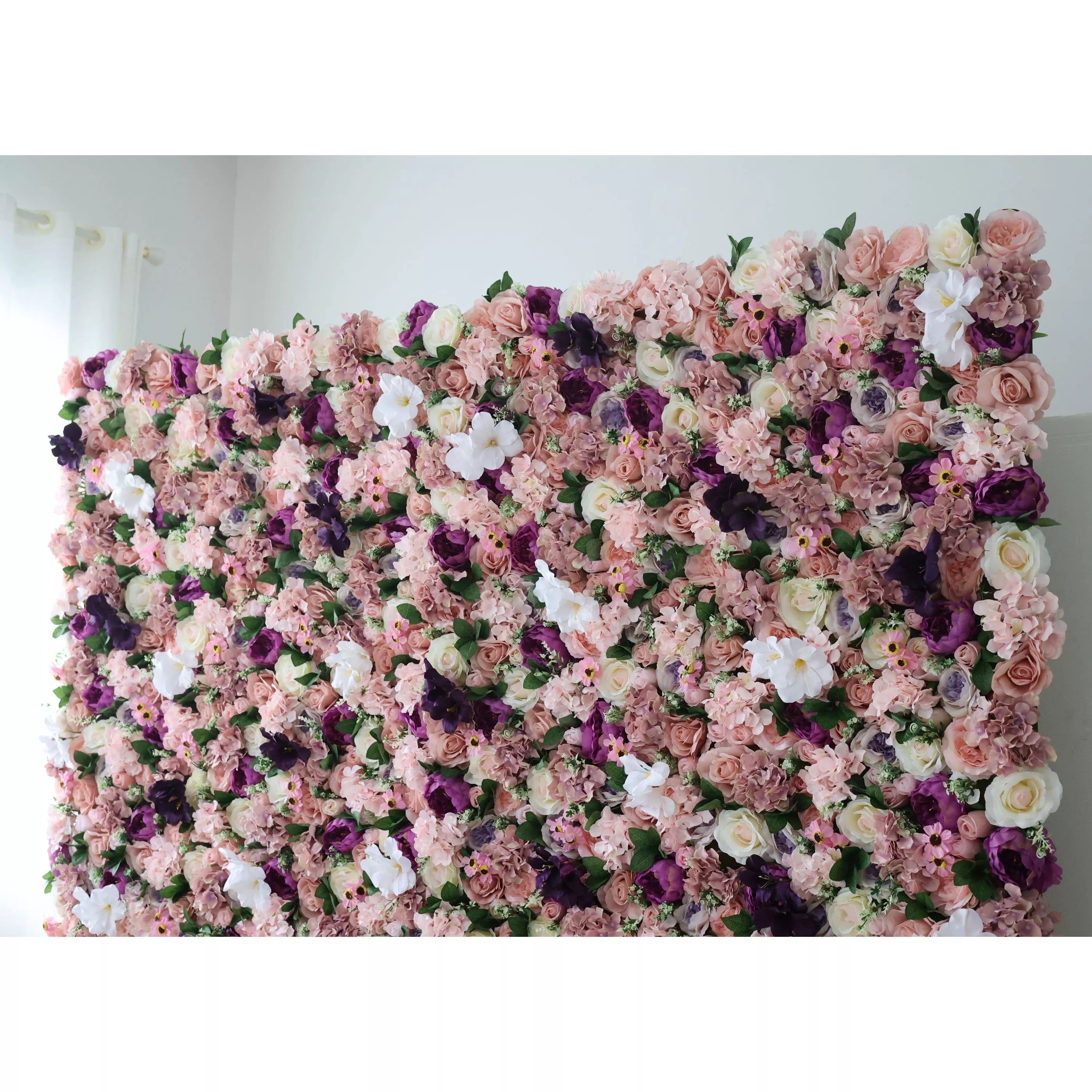 This opulent indoor floral backdrop features a dense, textured arrangement of artificial blooms in a romantic, vintage-inspired palette of blush, dusty rose, deep plum, and crisp white. The lush mix of roses, filler flowers, and subtle greenery creates a velvety, three-dimensional effect that exudes warmth and elegance. Set against a soft white wall, it serves as a sophisticated focal point for weddings, photoshoots, or upscale events.