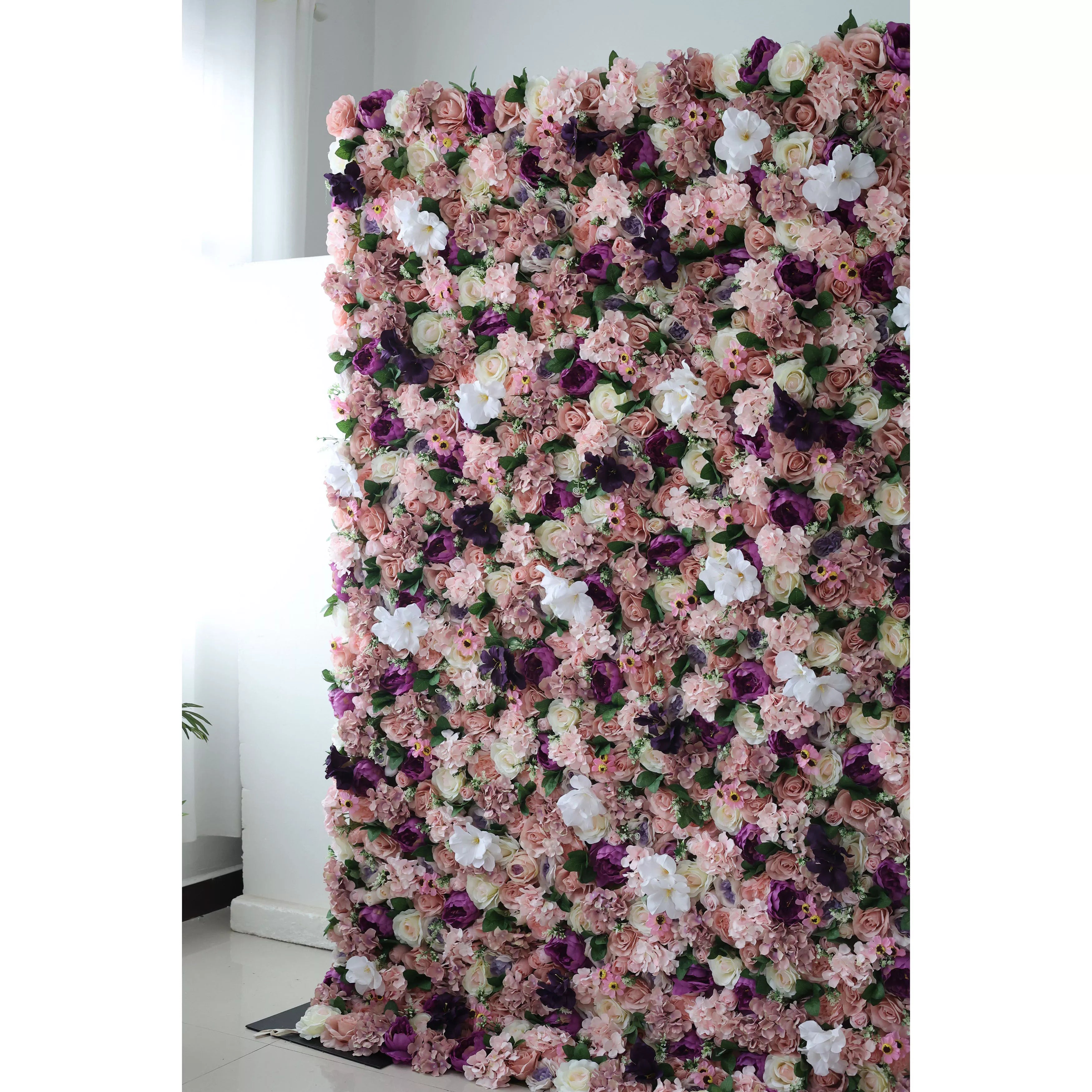 This elegant indoor floral backdrop features a dense, textured arrangement of artificial blooms in a romantic, vintage-inspired palette of blush, dusty rose, deep plum, and crisp white. The lush mix of roses and filler flowers creates a velvety, three-dimensional effect that exudes warmth and sophistication. Set against a minimalist white wall and light tiled floor, it serves as a stunning focal point for weddings, photoshoots, or upscale events.