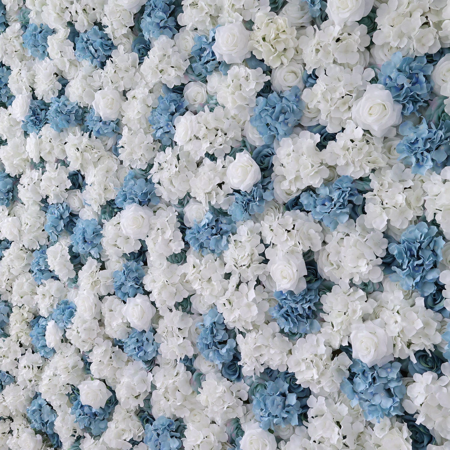 A dense wall of artificial flowers features a beautiful mix of white and blue blooms. Various floral types, including roses and hydrangeas, create a lush, elegant display. The cool color palette gives off a fresh, sophisticated vibe, perfect for events like weddings, parties, or as a decorative photo backdrop, adding a touch of refined charm to any setting.