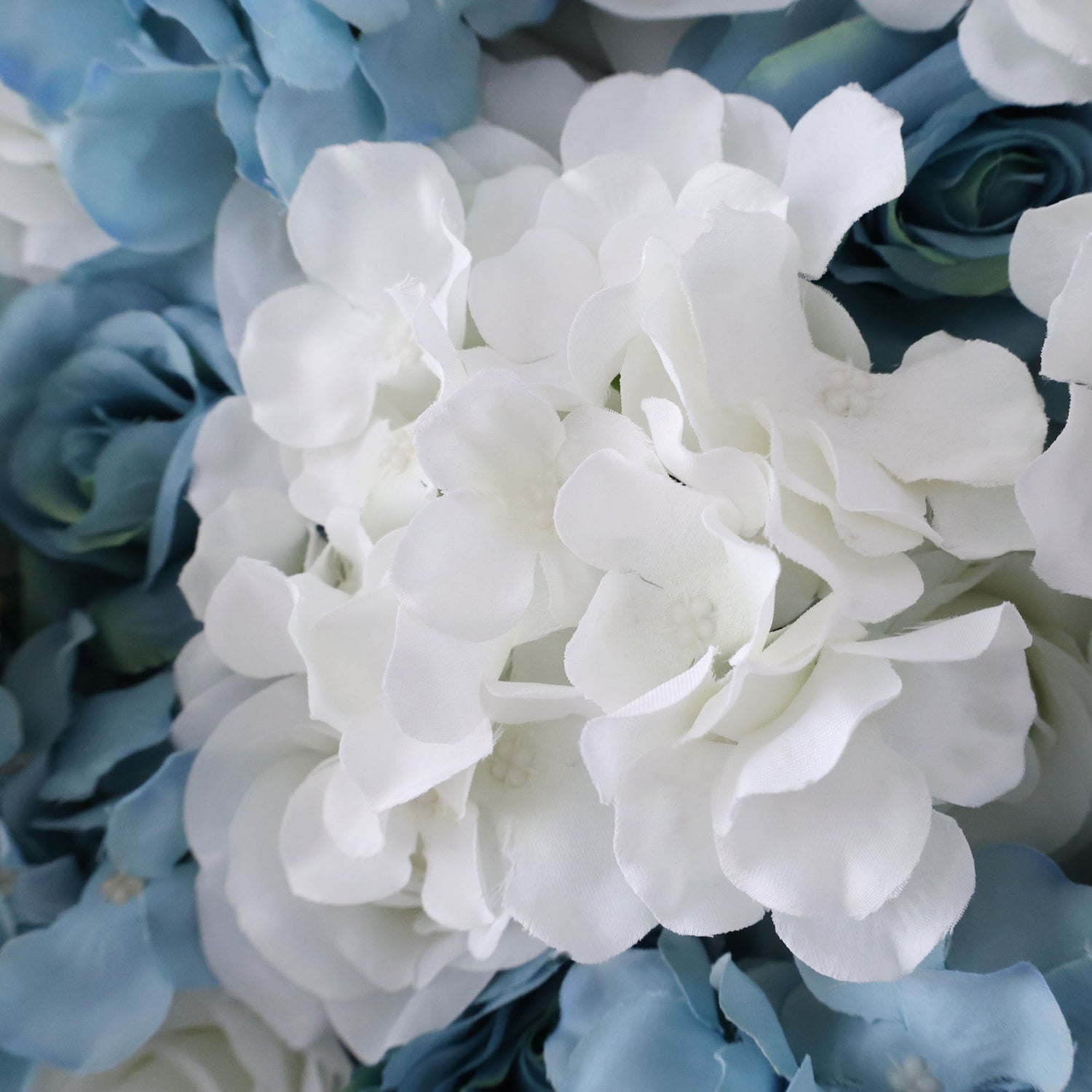 A close - up of artificial flowers showcases a beautiful mix of white and blue blooms. The white flowers, with their soft, layered petals, stand out prominently, while the blue flowers in the background add a cool contrast. The petals have a smooth, slightly glossy texture, giving the flowers a delicate and realistic appearance, ideal for decorative floral arrangements.