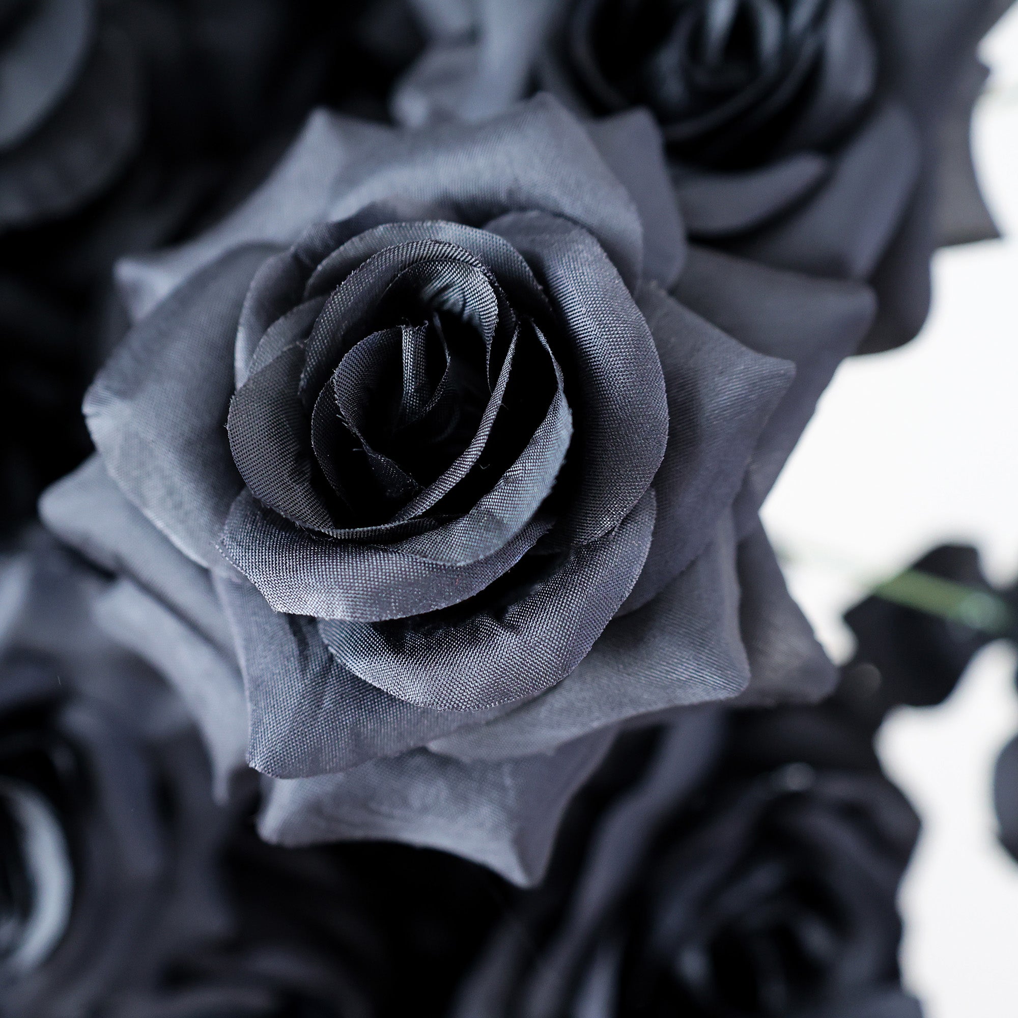 This photo showcases a close-up of artificial black roses, likely from ValarFlowers. The petals, crafted from fabric, mimic the delicate texture of real roses with a striking dark hue. The deep black color creates a dramatic, sophisticated aesthetic, perfect for avant-garde events or contemporary decor.  The detailed texture and rich color make it a captivating focal point, blending artistic design with the durability of artificial flowers.