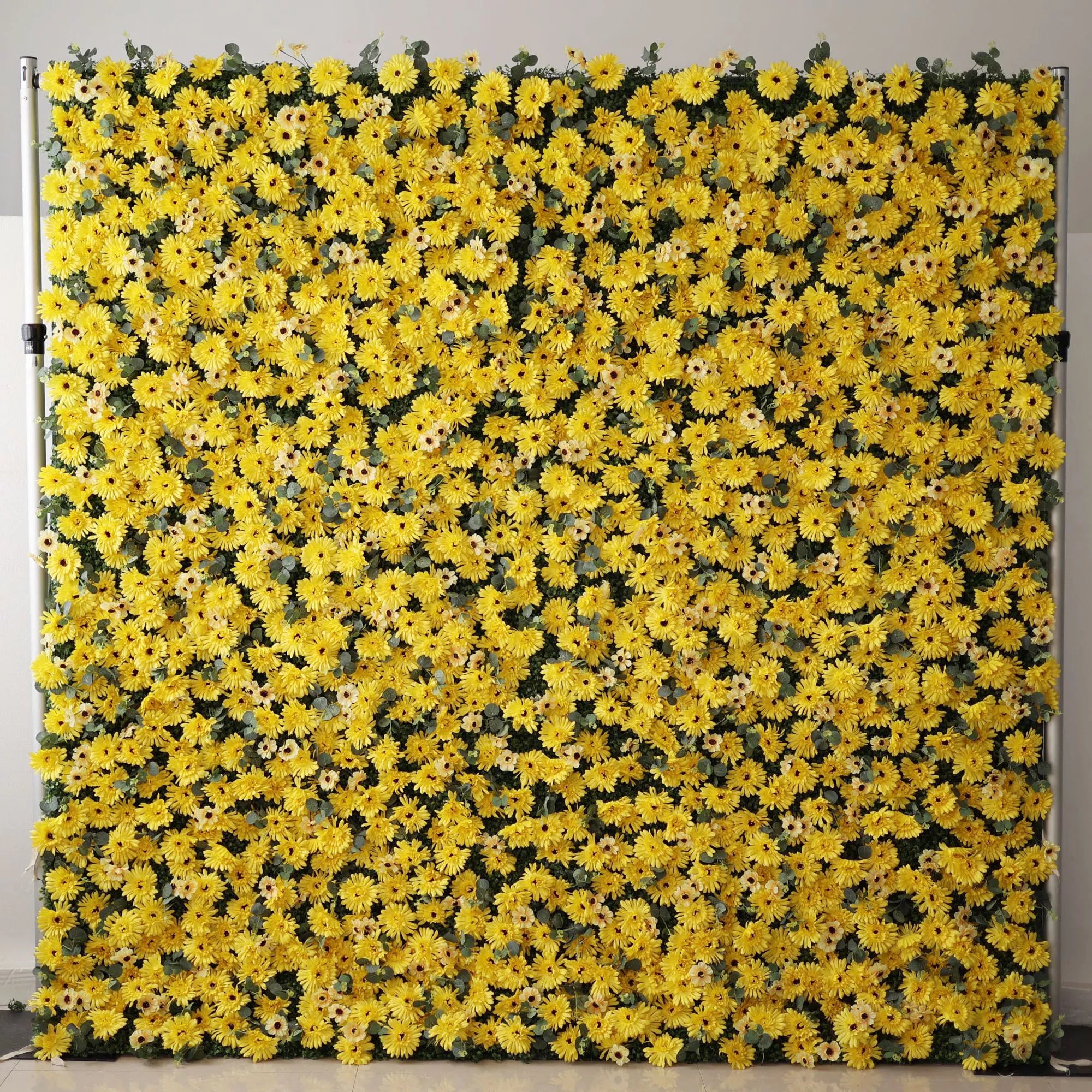 This vibrant indoor backdrop features a dense, wall-to-wall arrangement of artificial yellow daisies with dark centers, creating a cheerful, sun-drenched texture. The bold, monochromatic design exudes energy and warmth, punctuated by subtle hints of green foliage. Set against a minimalist white wall, it makes a lively focal point for summer events, photoshoots, or spaces seeking a bright, joyful aesthetic.