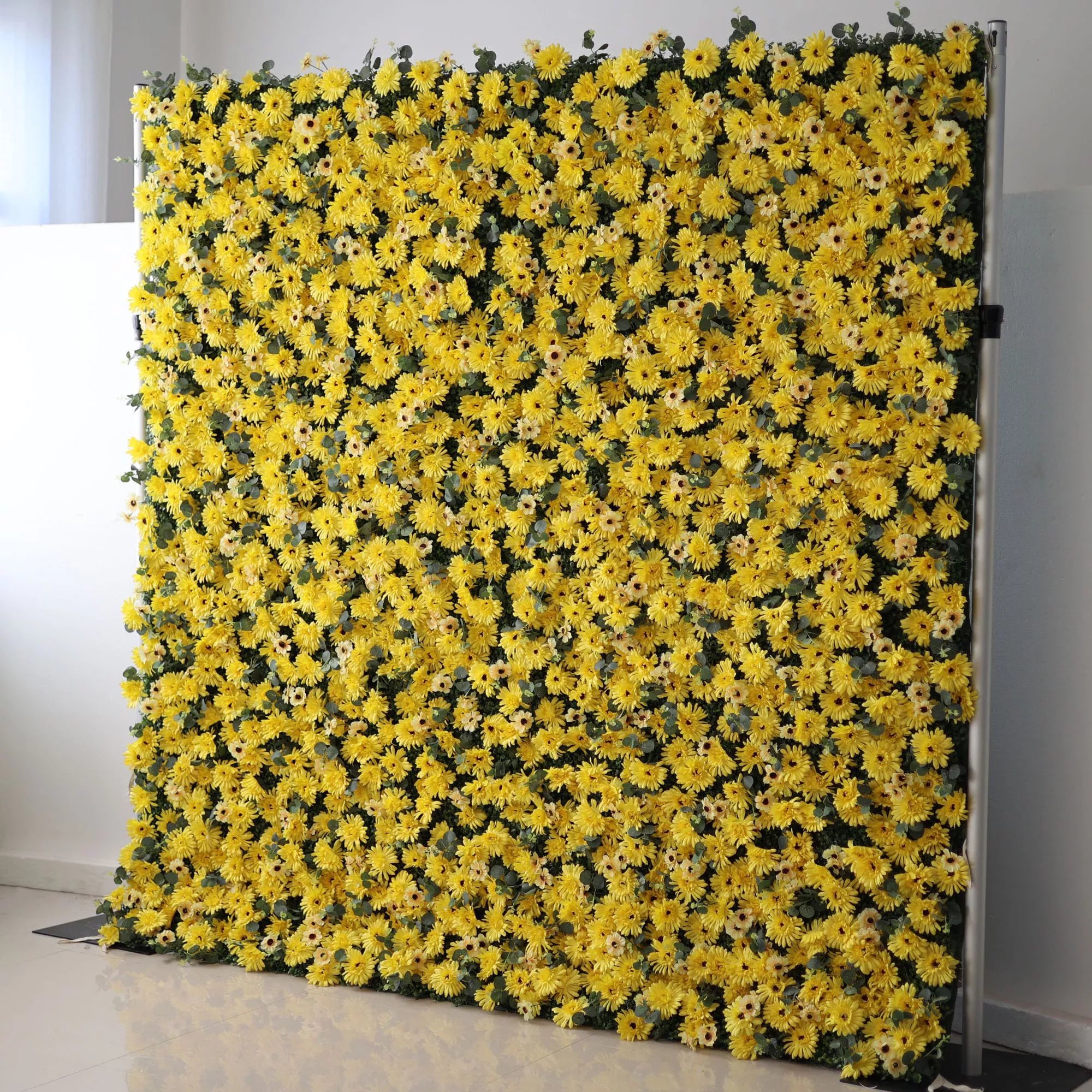 This vibrant indoor backdrop features a dense, wall-to-wall arrangement of artificial yellow daisies with dark centers, creating a cheerful, sun-drenched texture. Subtle green foliage peeks through the blooms, adding depth to the bold, monochromatic design. Set against a minimalist white wall and light tiled floor, it exudes energy and warmth, making it a lively focal point for summer events, photoshoots, or spaces seeking a bright, joyful aesthetic.