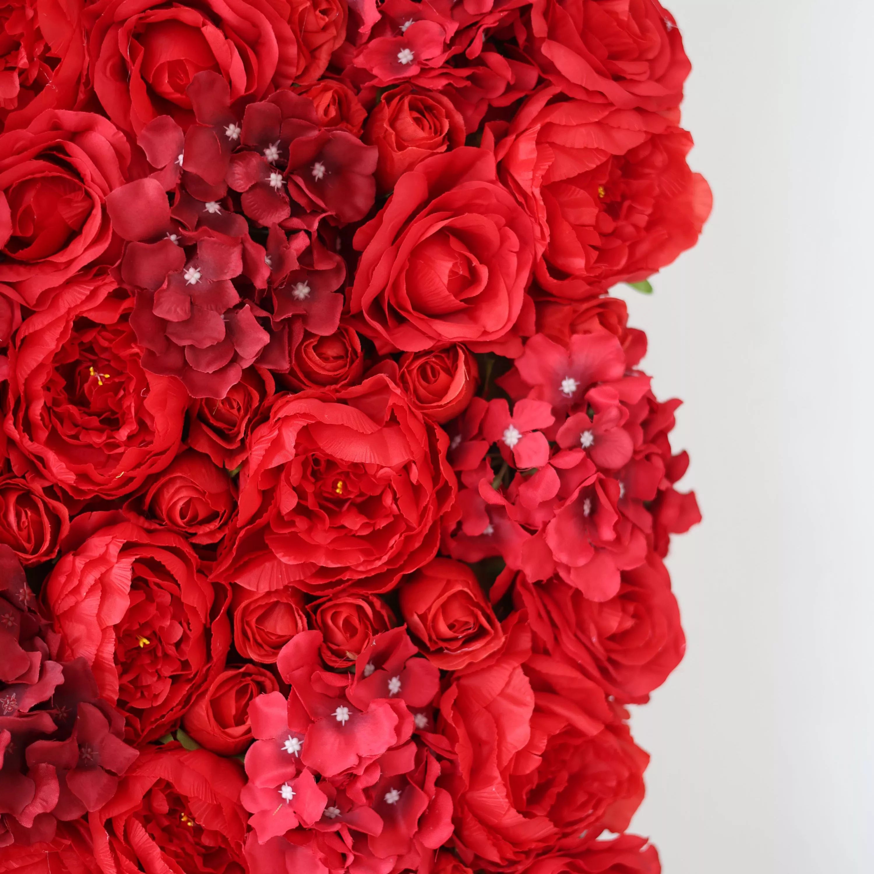 This close-up showcases a dense, textured arrangement of artificial red blooms, featuring lush, ruffled roses and clustered hydrangeas with subtle white accents at their centers. The rich, saturated red palette creates a bold, romantic display, ideal for event backdrops, photo booths, or interior decor seeking a dramatic, passionate focal point. The artificial construction ensures long-lasting vibrancy and consistent texture.