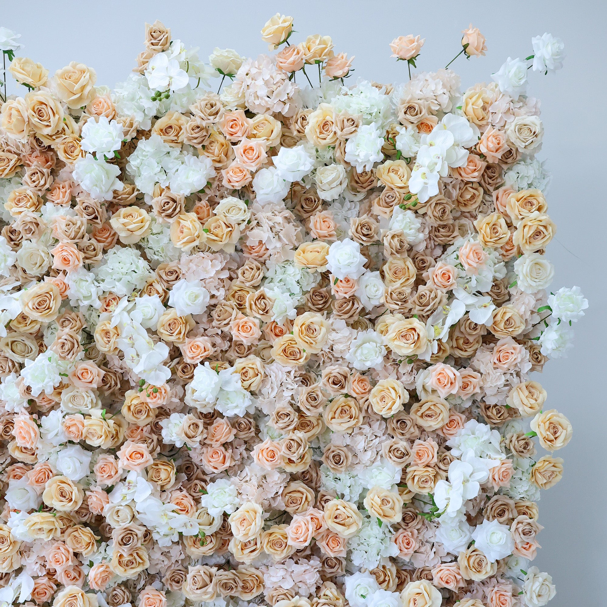 This image features a dense, vibrant arrangement of artificial flowers in soft hues of beige, white, and light pink. The flowers, including roses and other blooms, are clustered tightly to form a lush, romantic floral tapestry. Set against a plain backdrop, the intricate petals and harmonious color palette create an elegant, charming scene, ideal for event decor or as a visually appealing artistic display.
