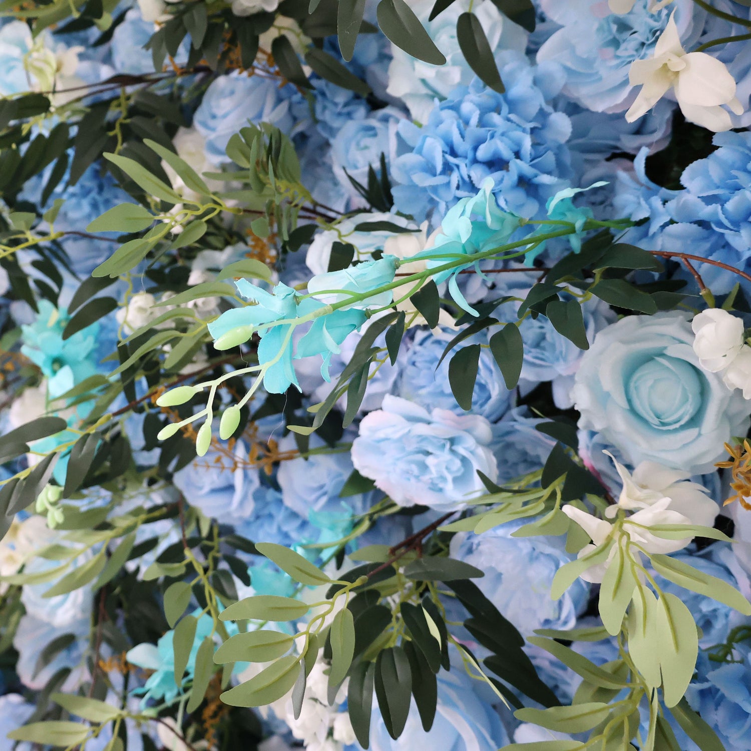 This image showcases a beautiful floral wall by Valar Flowers. It features a dense arrangement of artificial flowers in various shades of blue, from light sky blue to deeper hues, along with some white blooms. Lush green foliage is interspersed, creating a lush, serene, and visually captivating display. Perfect for adding an elegant, nature - inspired touch to events or interior spaces, it exudes a sense of tranquility and beauty.