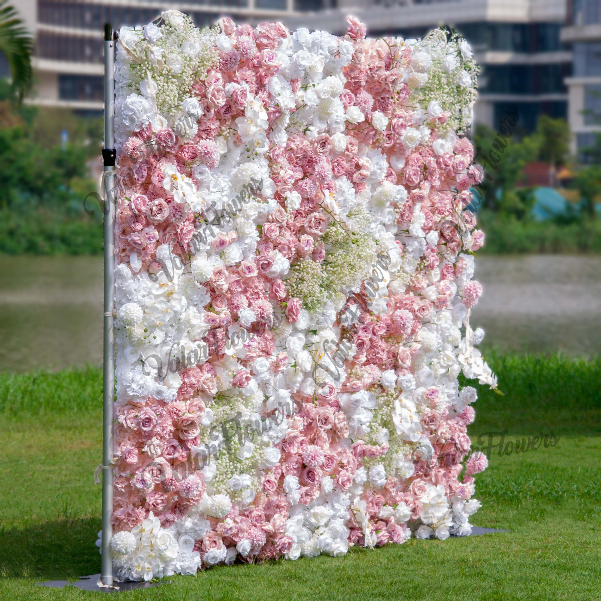 This backdrop is a vibrant floral wall supported by a metal frame. It features a mix of artificial flowers, including roses in soft pinks and whites, white hydrangeas, and clusters of baby&